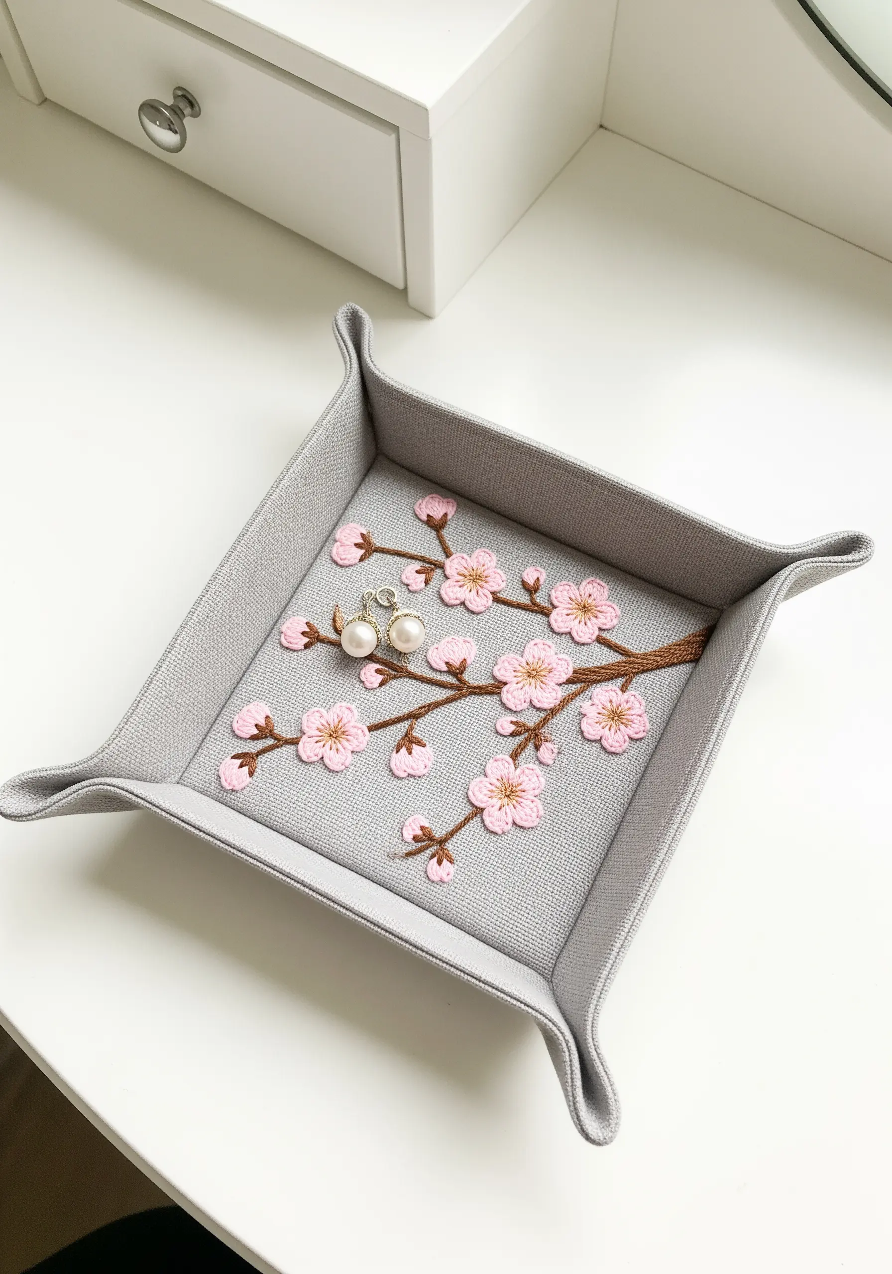 A gray fabric valet tray embroidered with a delicate branch of pink cherry blossoms.