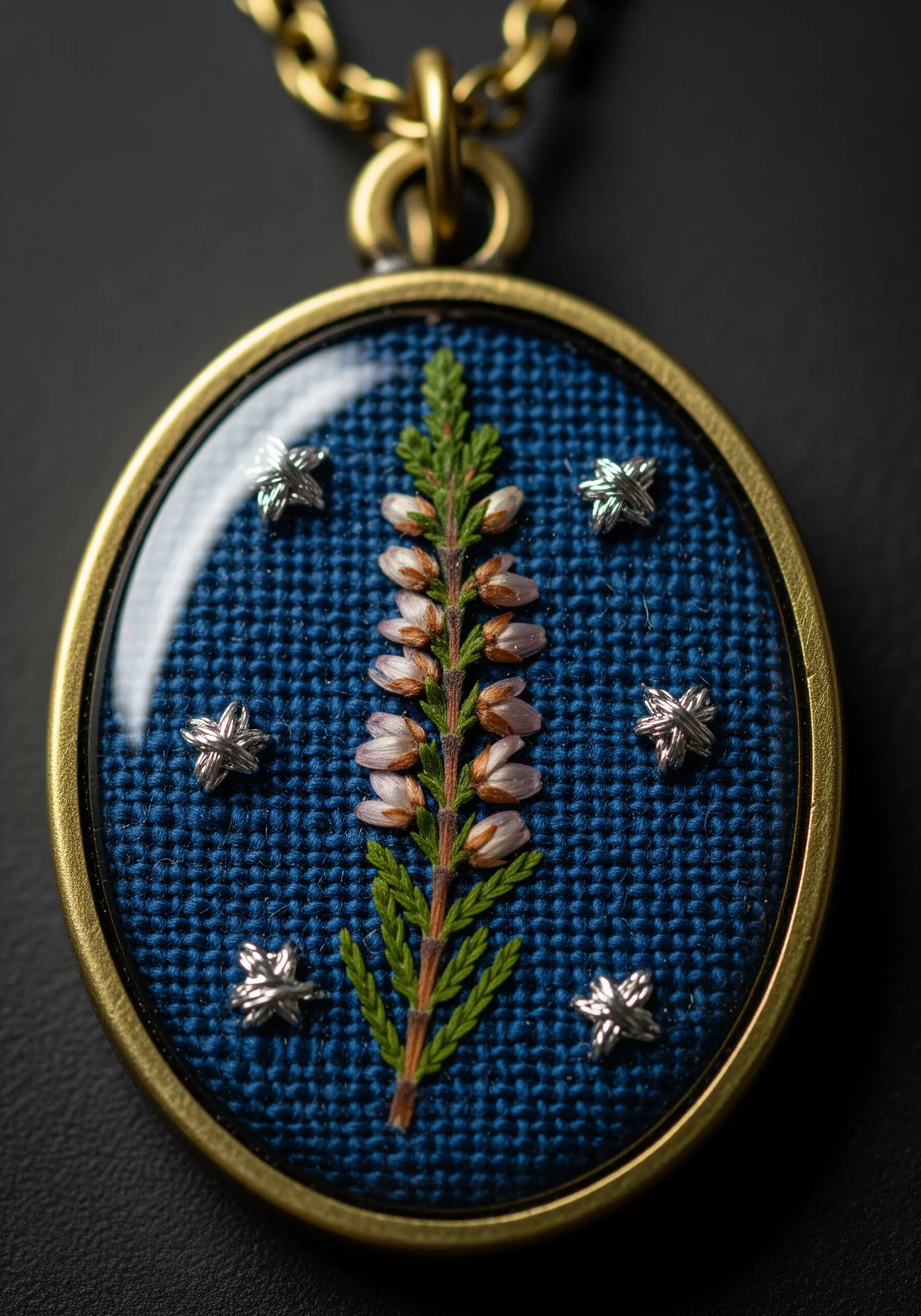 A close-up of an embroidery pendant with a pressed heather sprig and tiny silver star stitches.