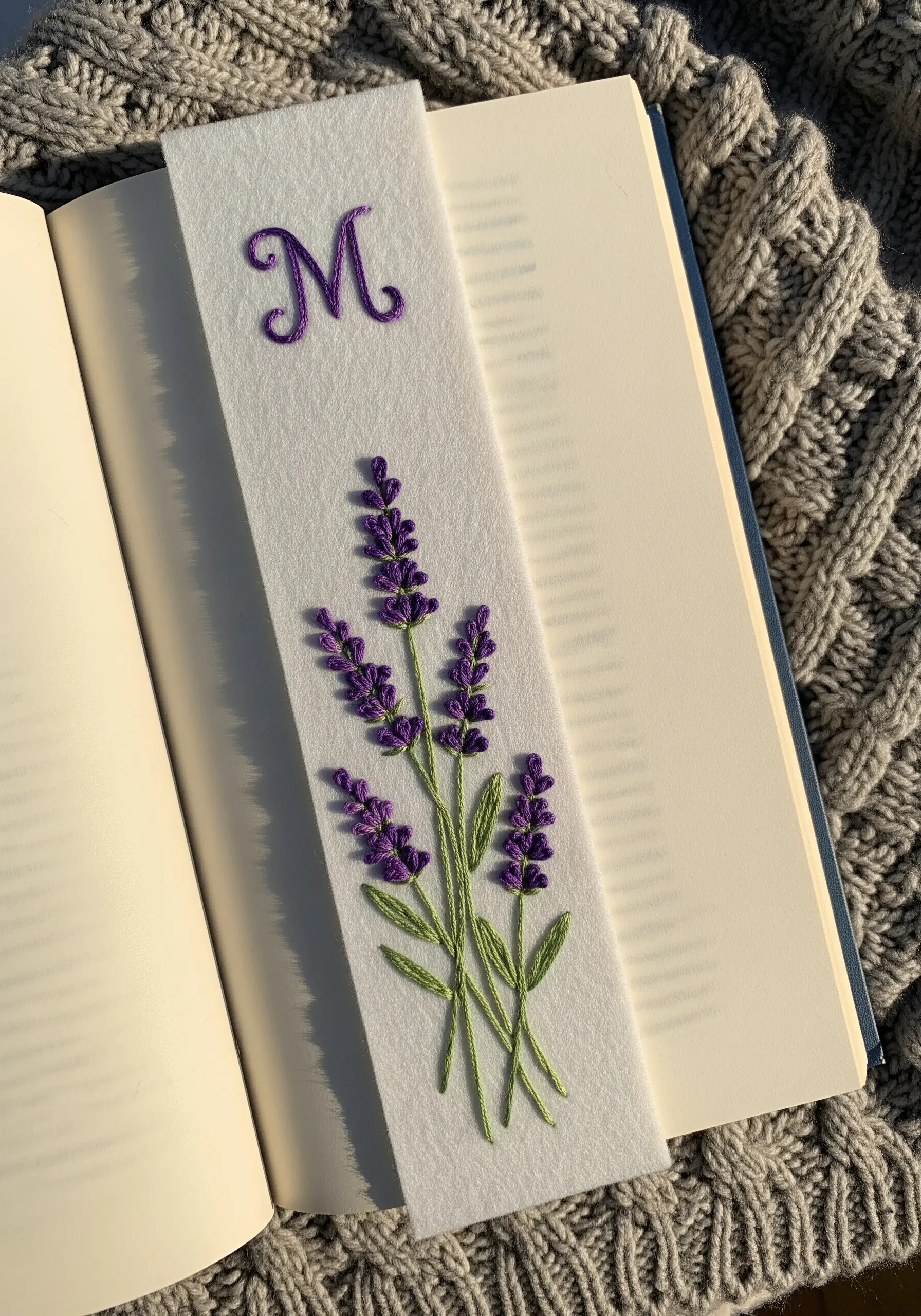 A white felt bookmark embroidered with a lavender sprig and the initial 'M'.
