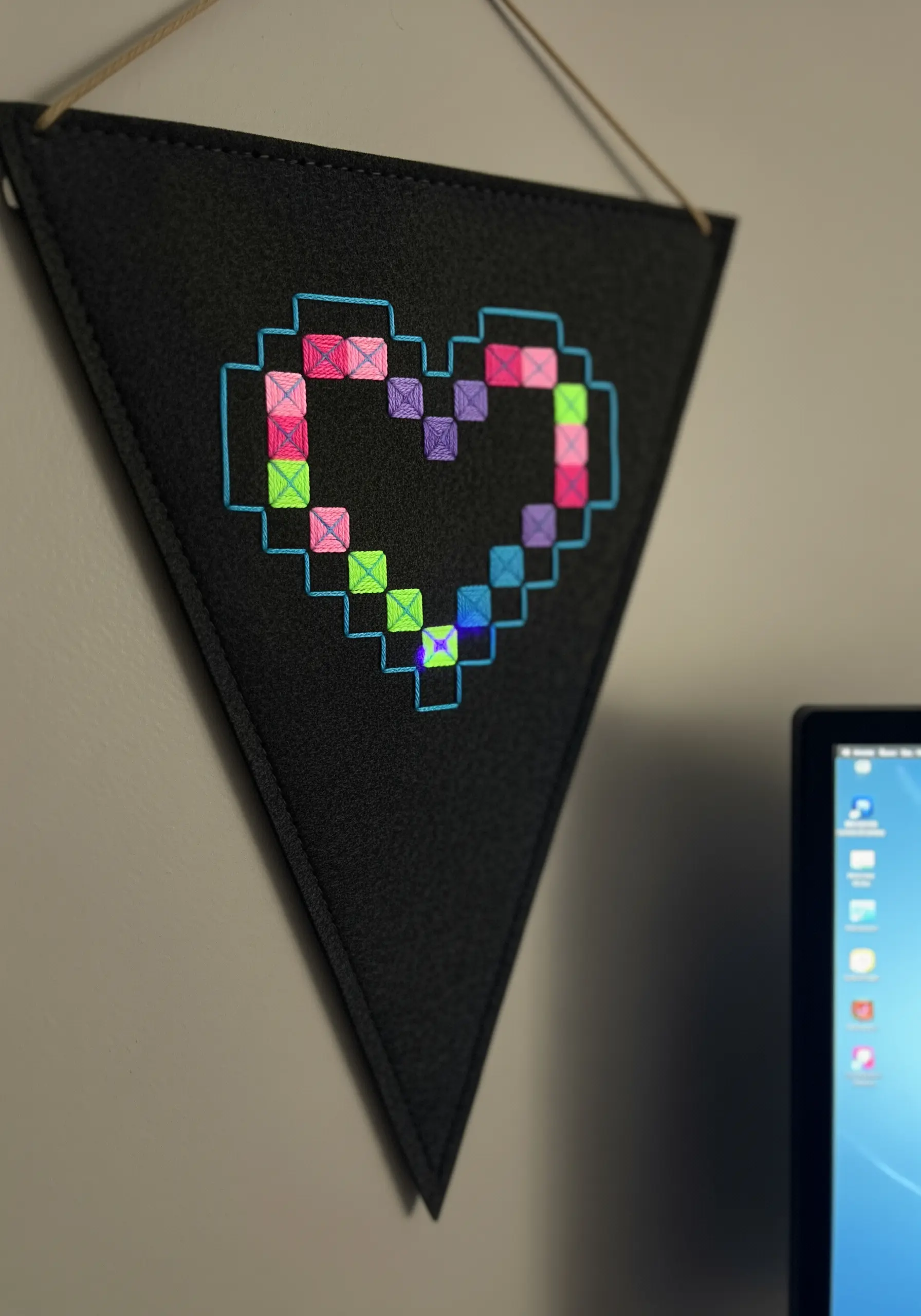 Embroidered pixelated heart in neon colors on a black felt pennant.