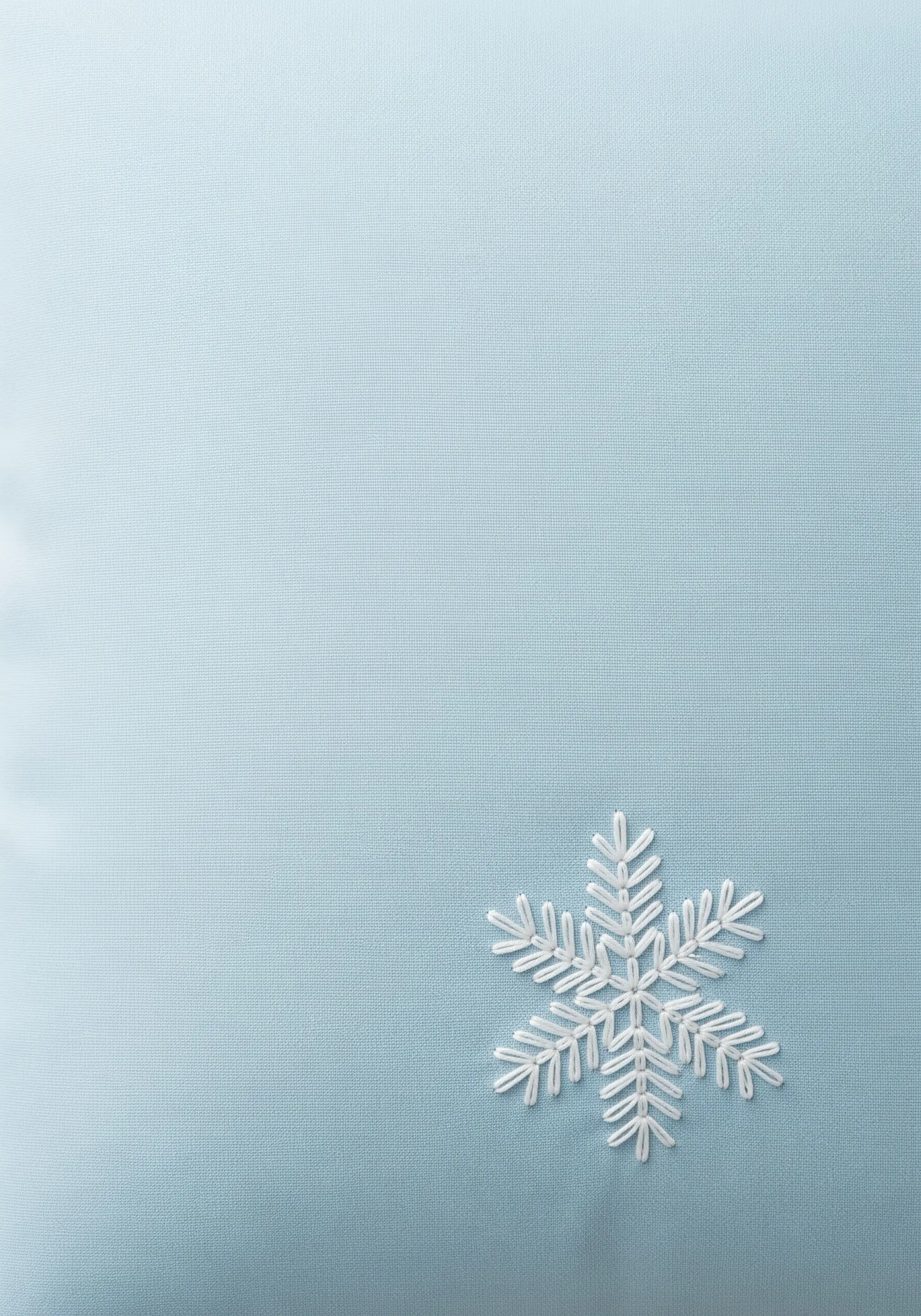 A single, symmetrical snowflake embroidered in white thread on a light blue pillowcase.