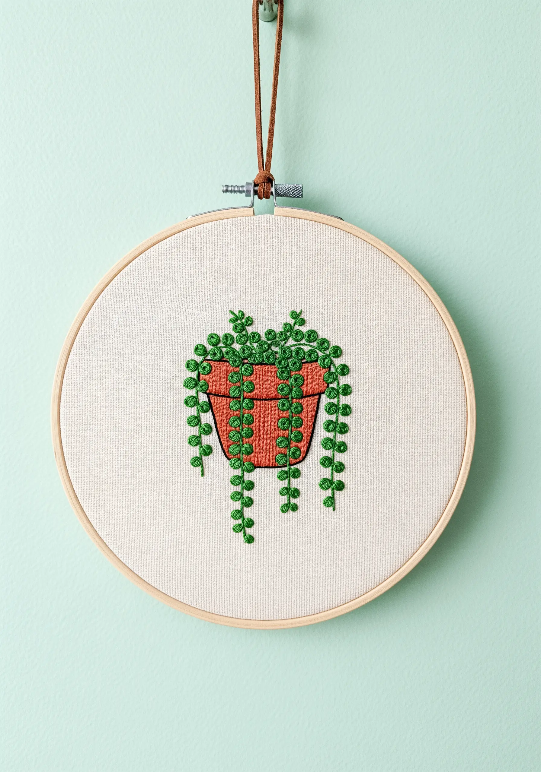 Embroidered string of pearls plant in a terracotta pot hanging in a hoop.