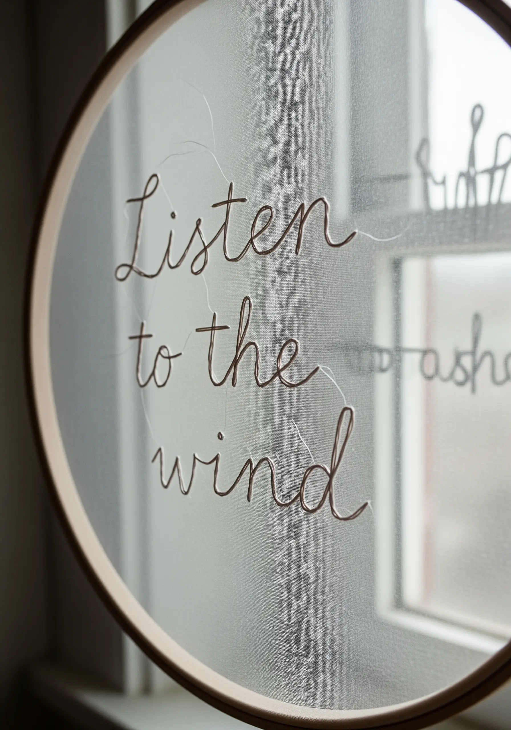 Delicate cursive script embroidered on a sheer, transparent fabric in a hoop.