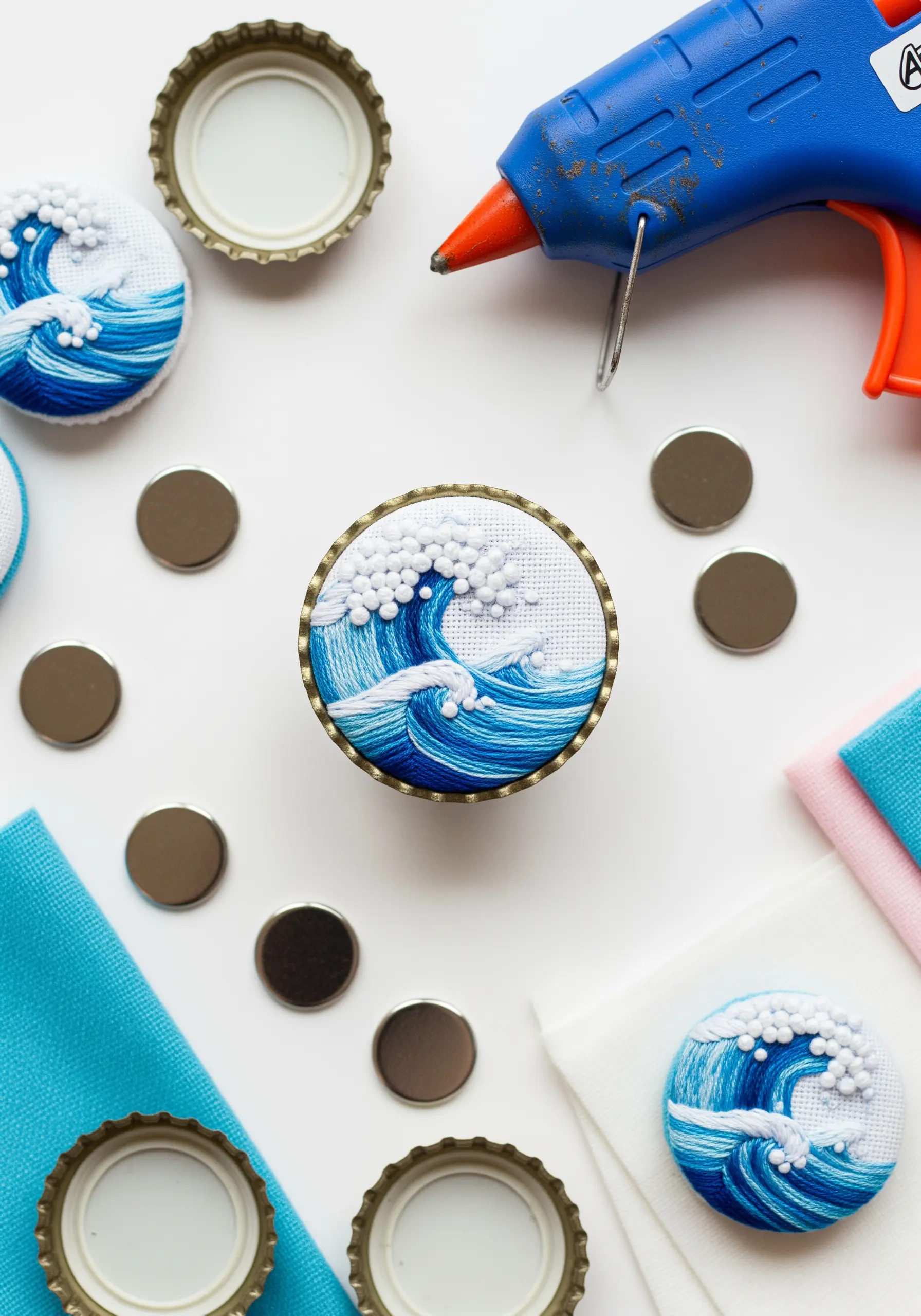 A tiny embroidered ocean wave with French knot foam, set inside a bottle cap magnet.