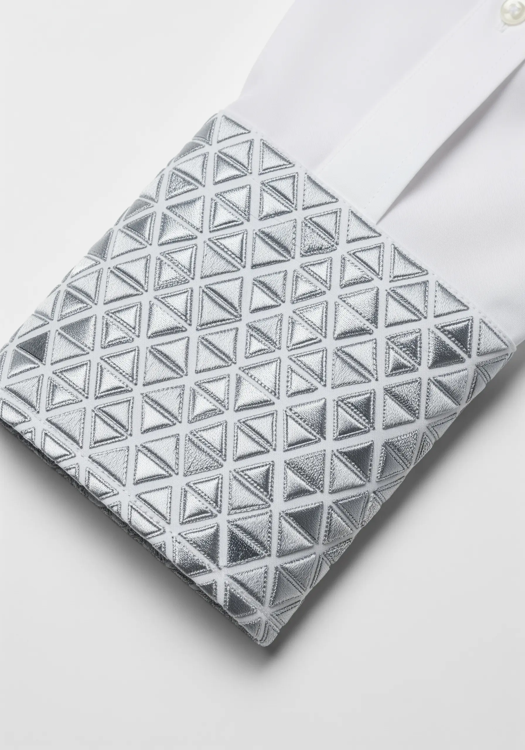 A white shirt cuff heavily embroidered with a 3D geometric pattern in silver metallic thread.