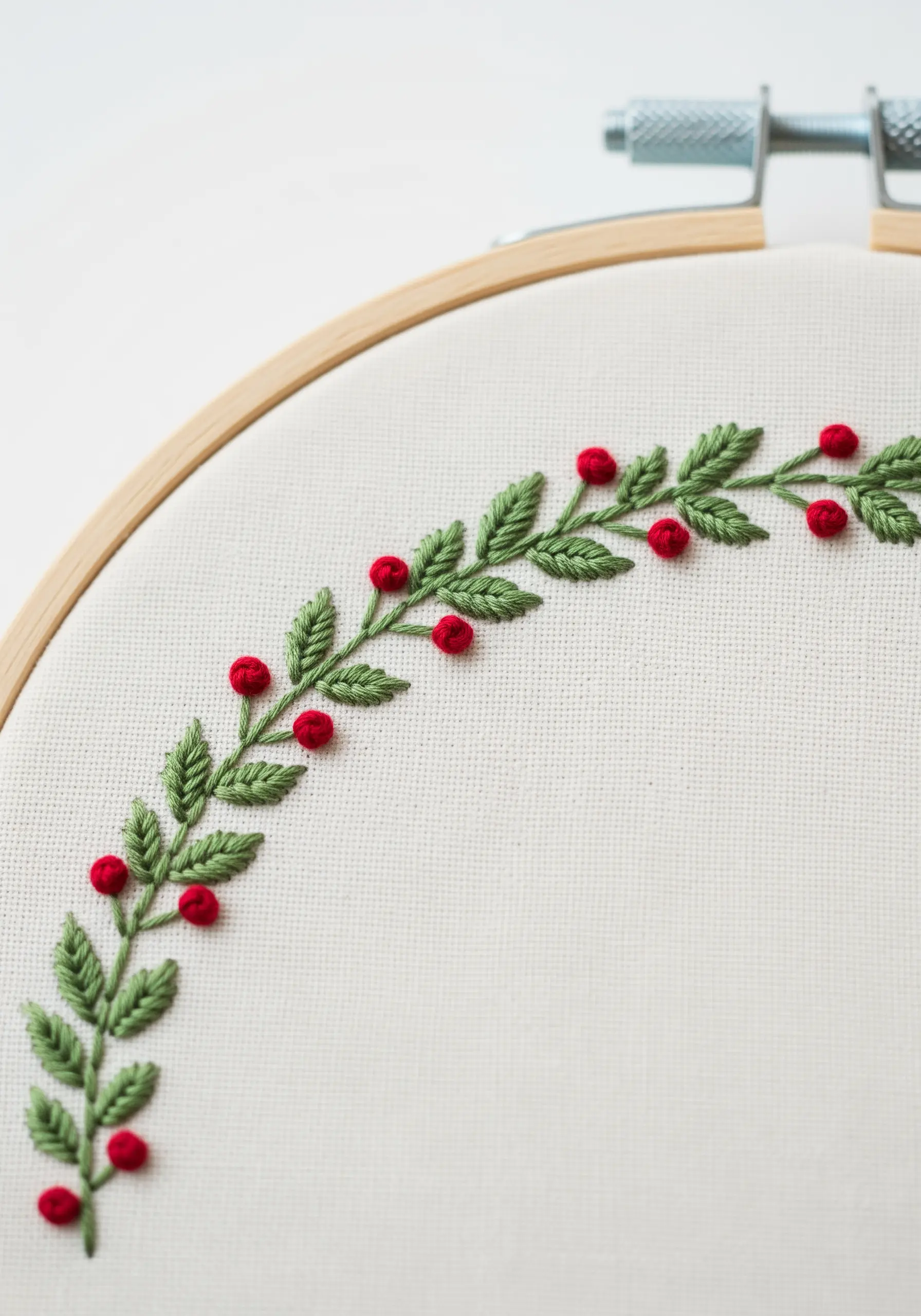 A delicate embroidered border of a holly branch with green leaves and red berries.