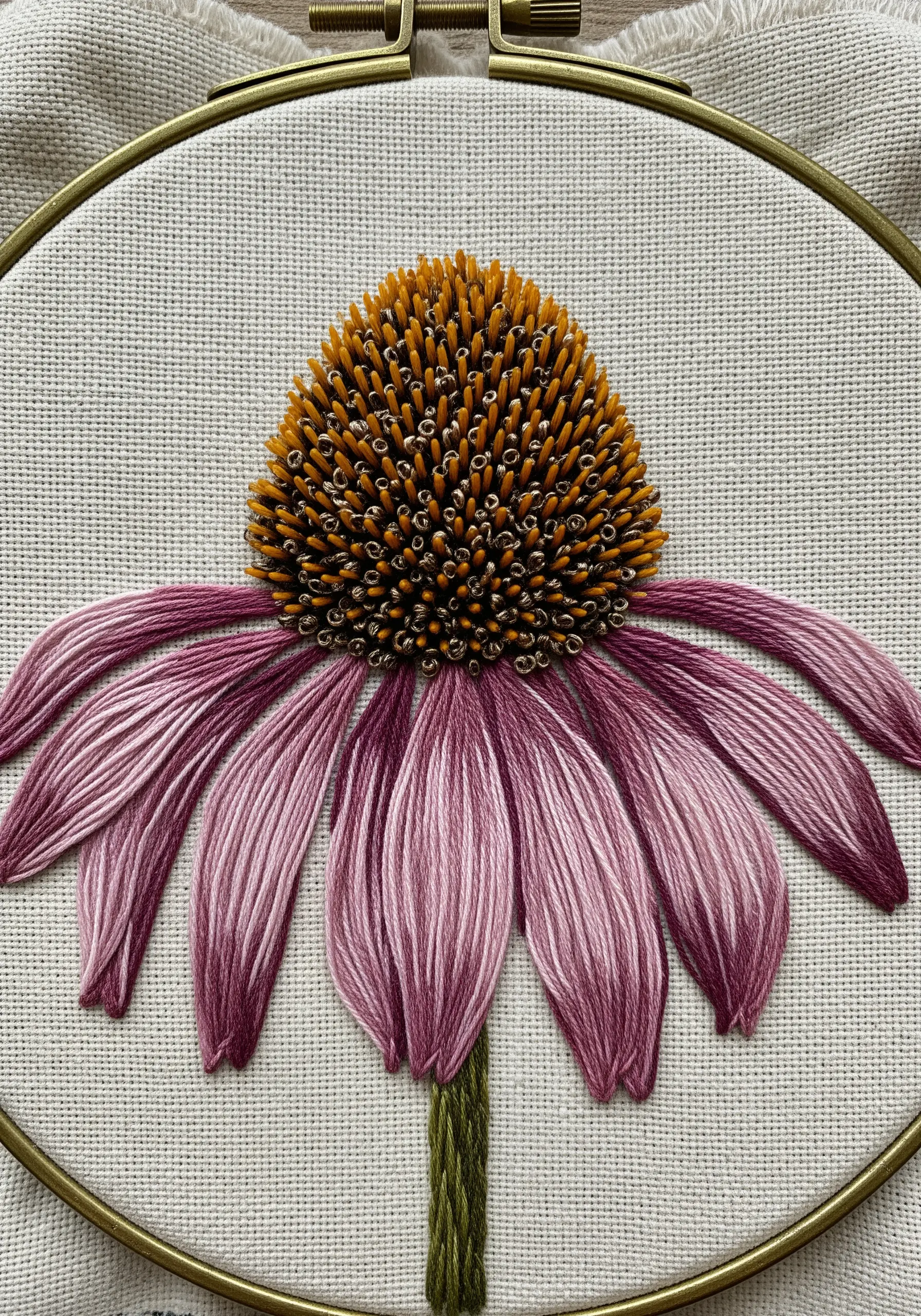 Close-up of an embroidered echinacea with a textured French knot center and pink petals.