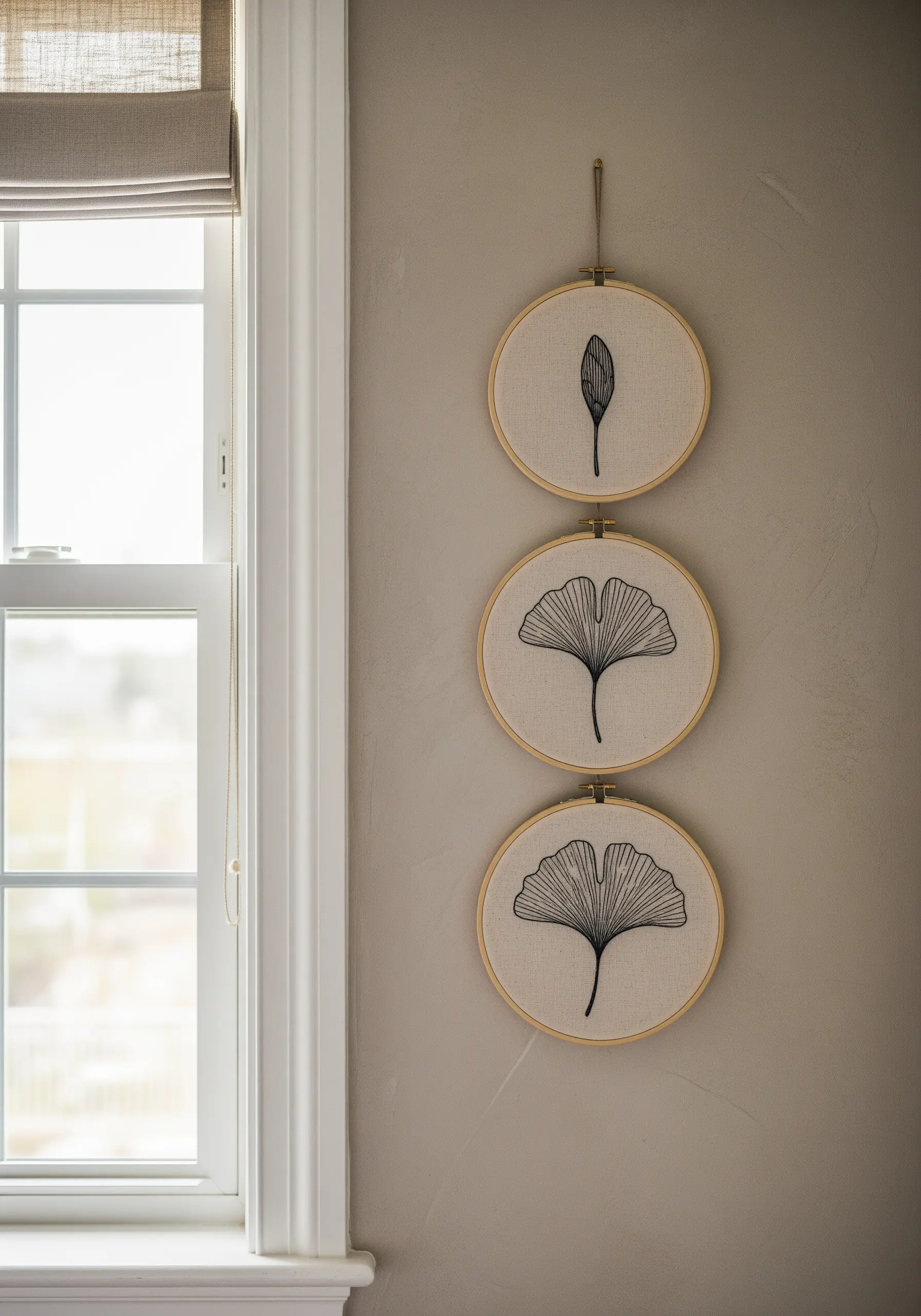 A vertical triptych of three embroidery hoops showing the growth stages of a ginkgo leaf.