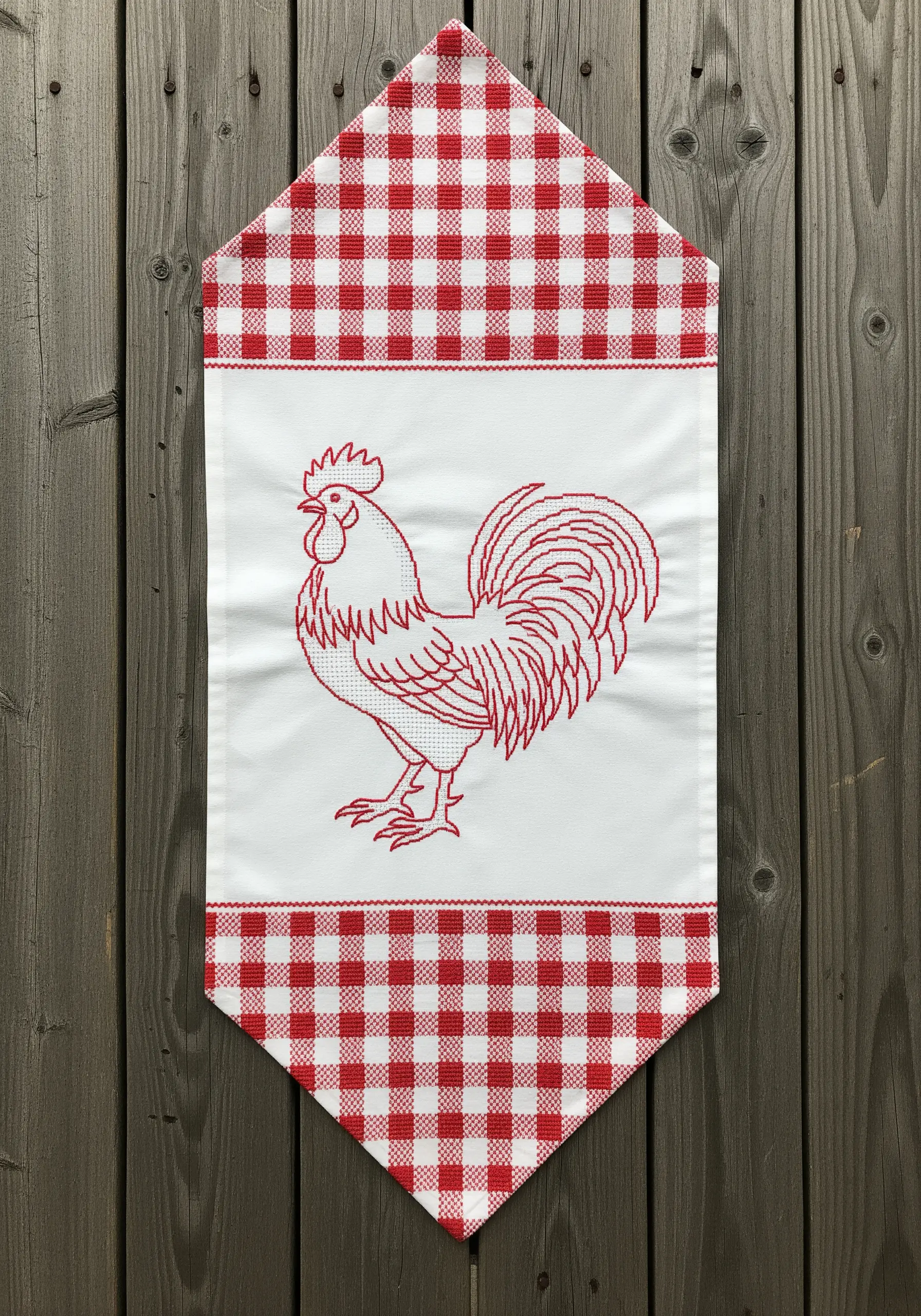 A table runner featuring a redwork embroidered rooster on a white panel, framed with red gingham.