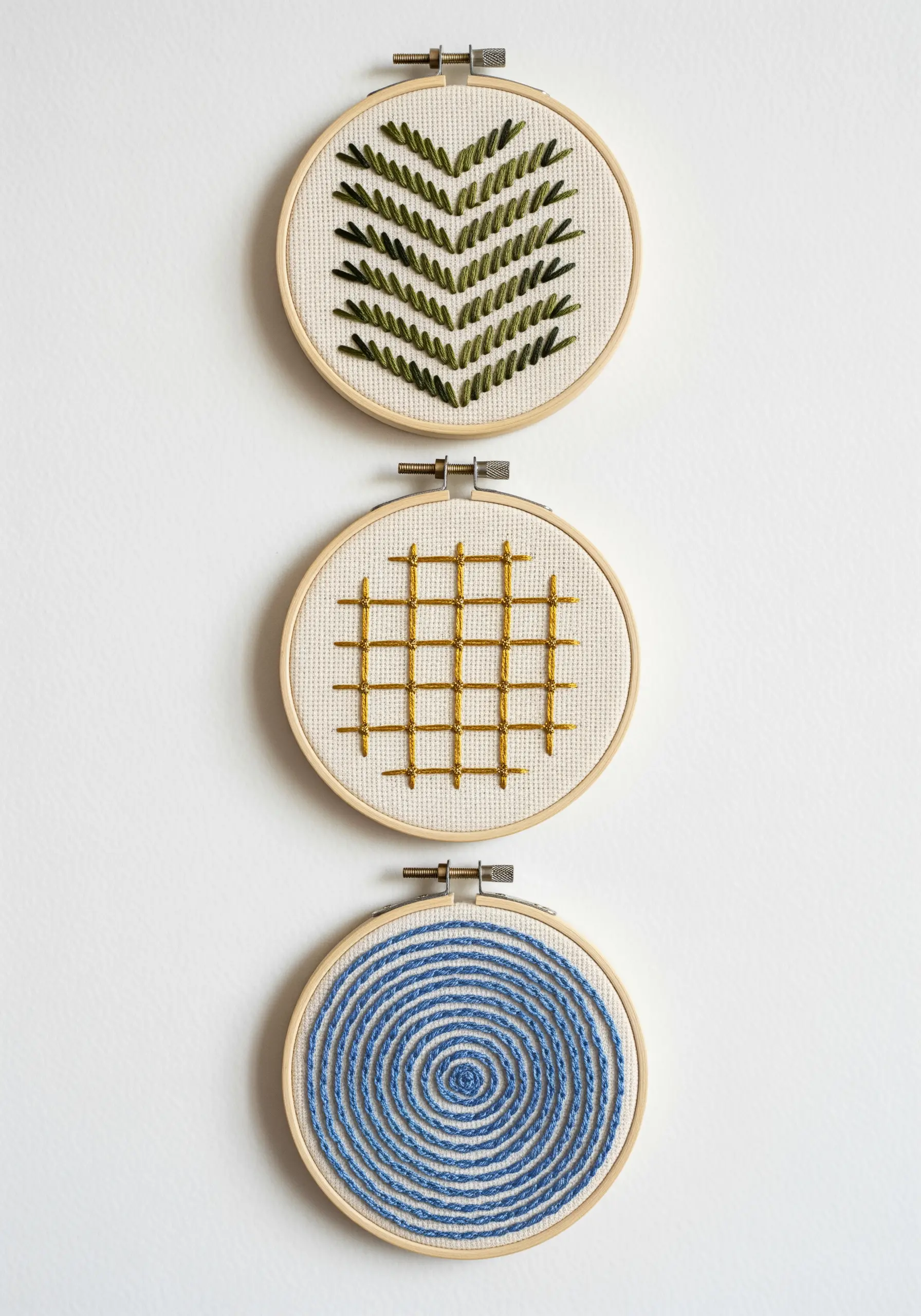 Three small hoops with abstract patterns: leaf, grid, and spiral stitches.