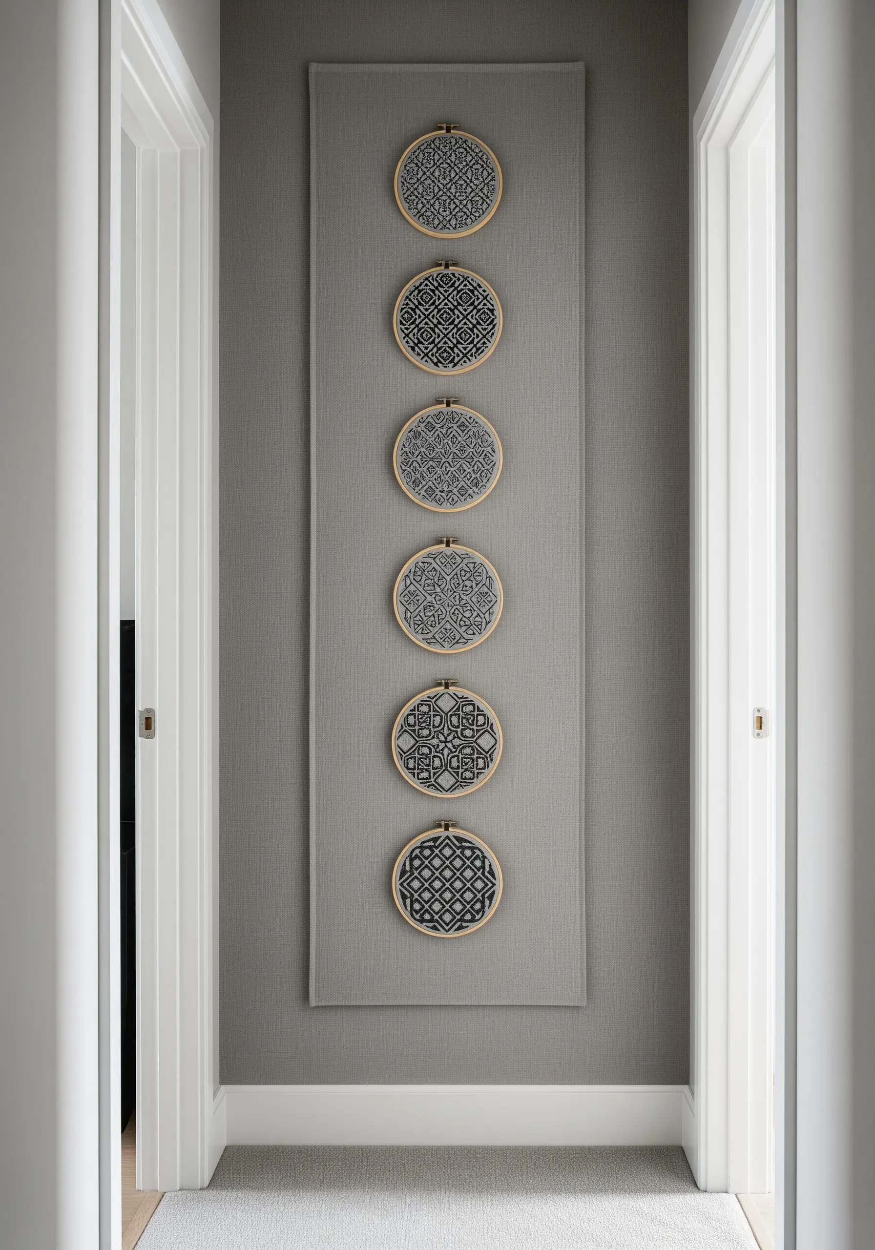A vertical fabric runner hanging in a hallway with five small hoops of monochrome patterns.