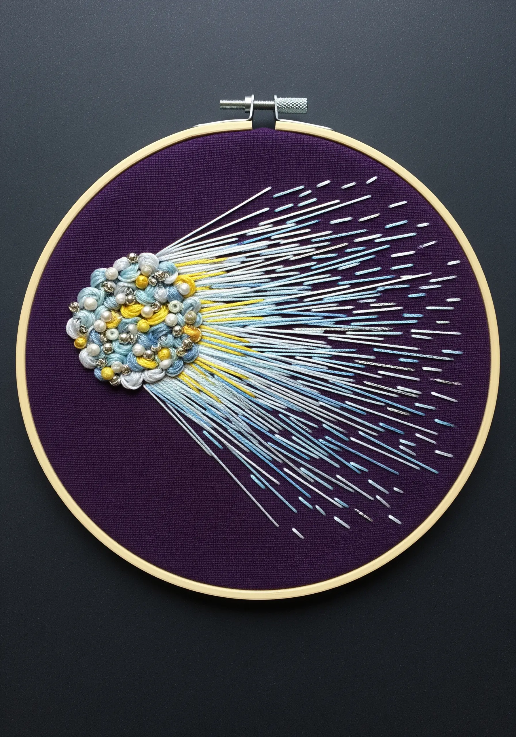 An abstract beaded and embroidered comet with a long, trailing tail on purple fabric.