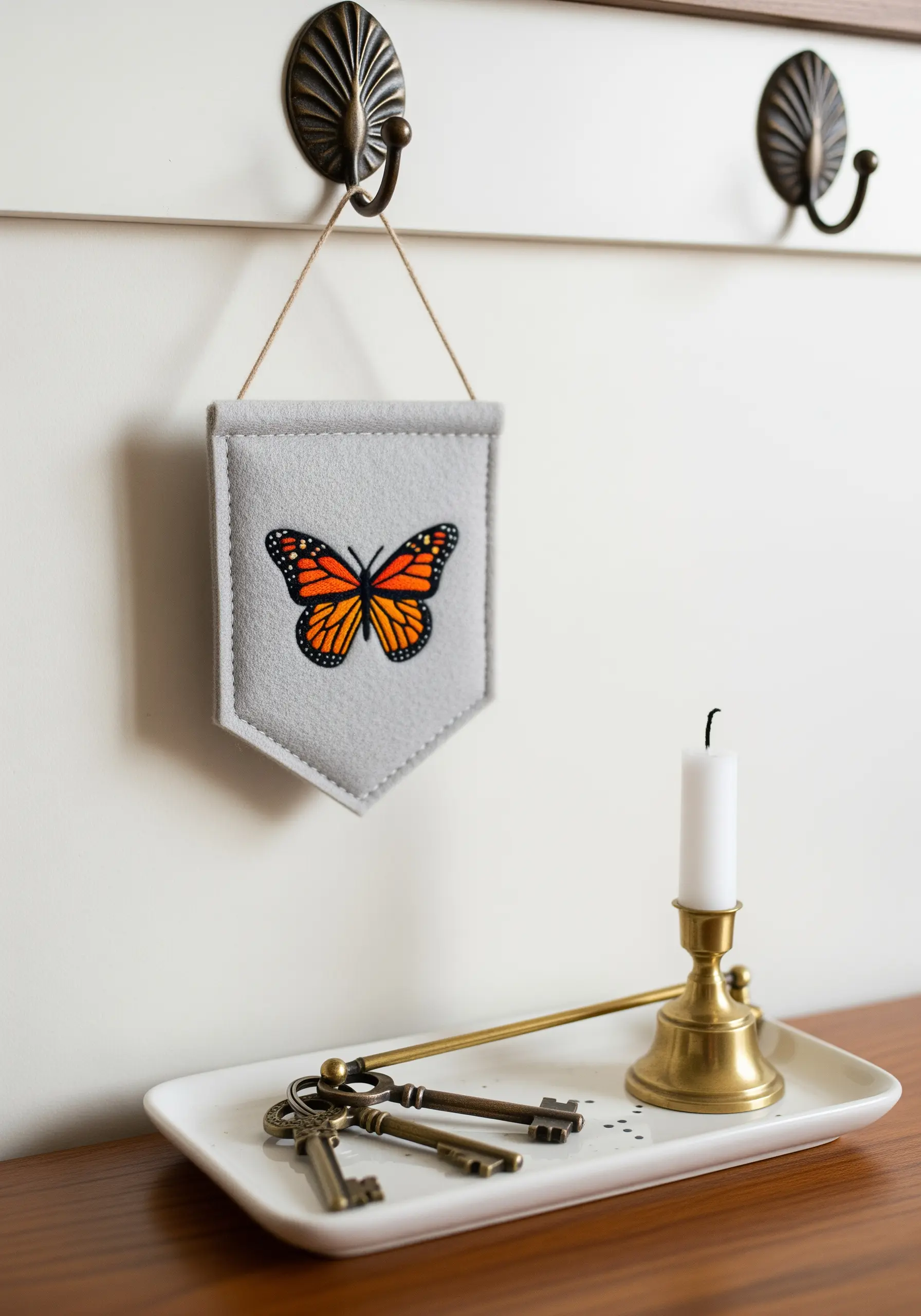 Embroidered monarch butterfly with blended orange and yellow wings on a gray felt banner.