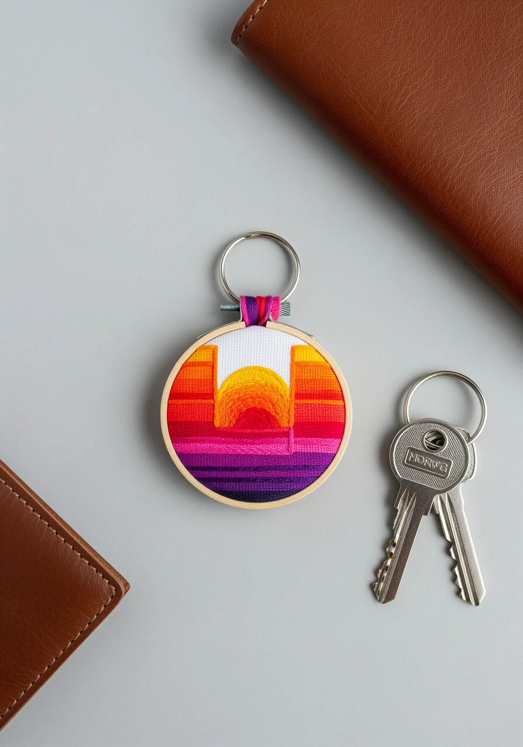 A tiny embroidery hoop keychain with a vibrant, geometric sunset design.