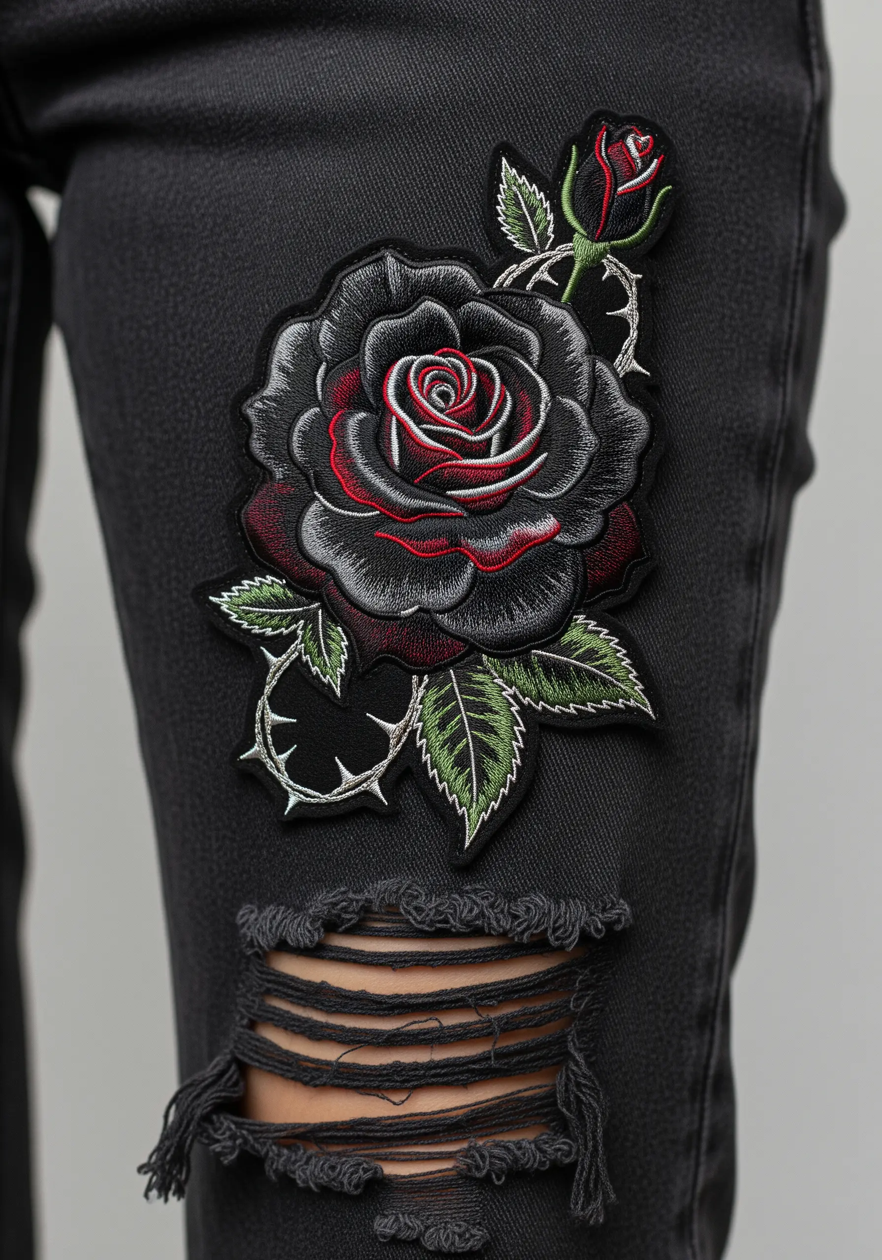 A gothic-style black rose patch with red and grey highlights on ripped black jeans.