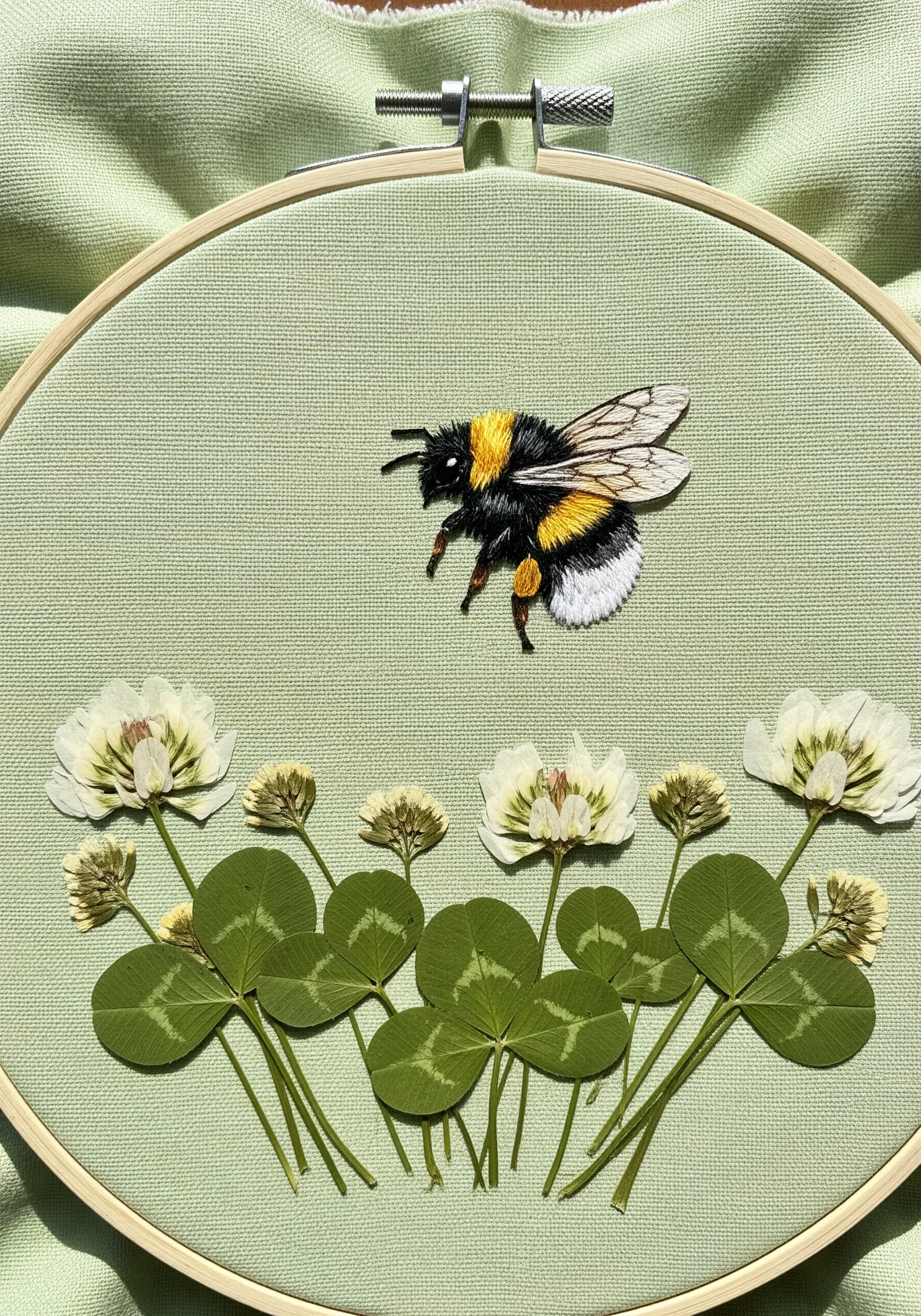 Thread-painted bumblebee hovering over a field of pressed clover.