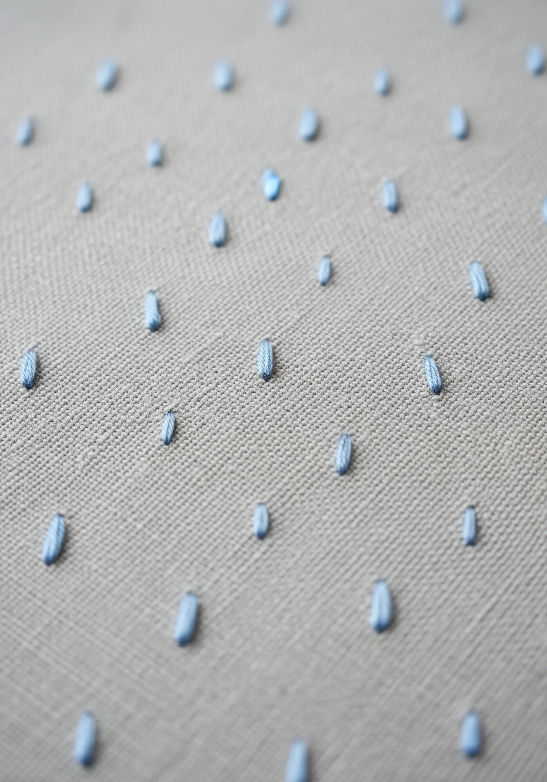 A gray fabric with a repeating pattern of small, vertical blue stitches.