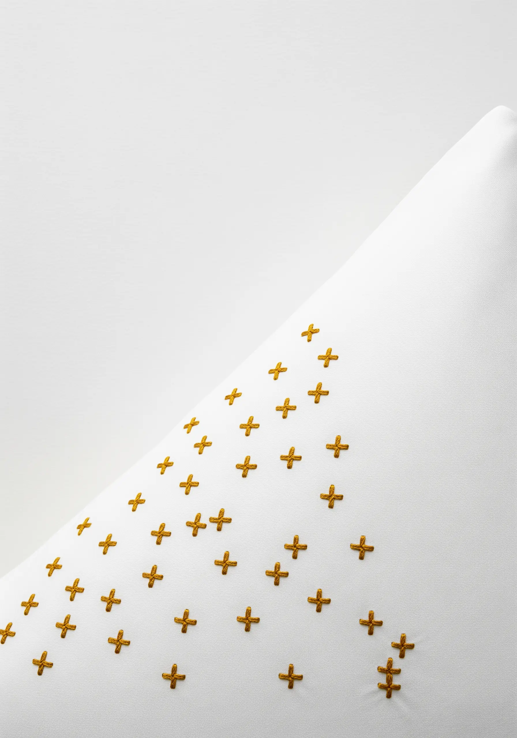 A pattern of small, mustard-yellow cross stitches on the corner of a white pillowcase.
