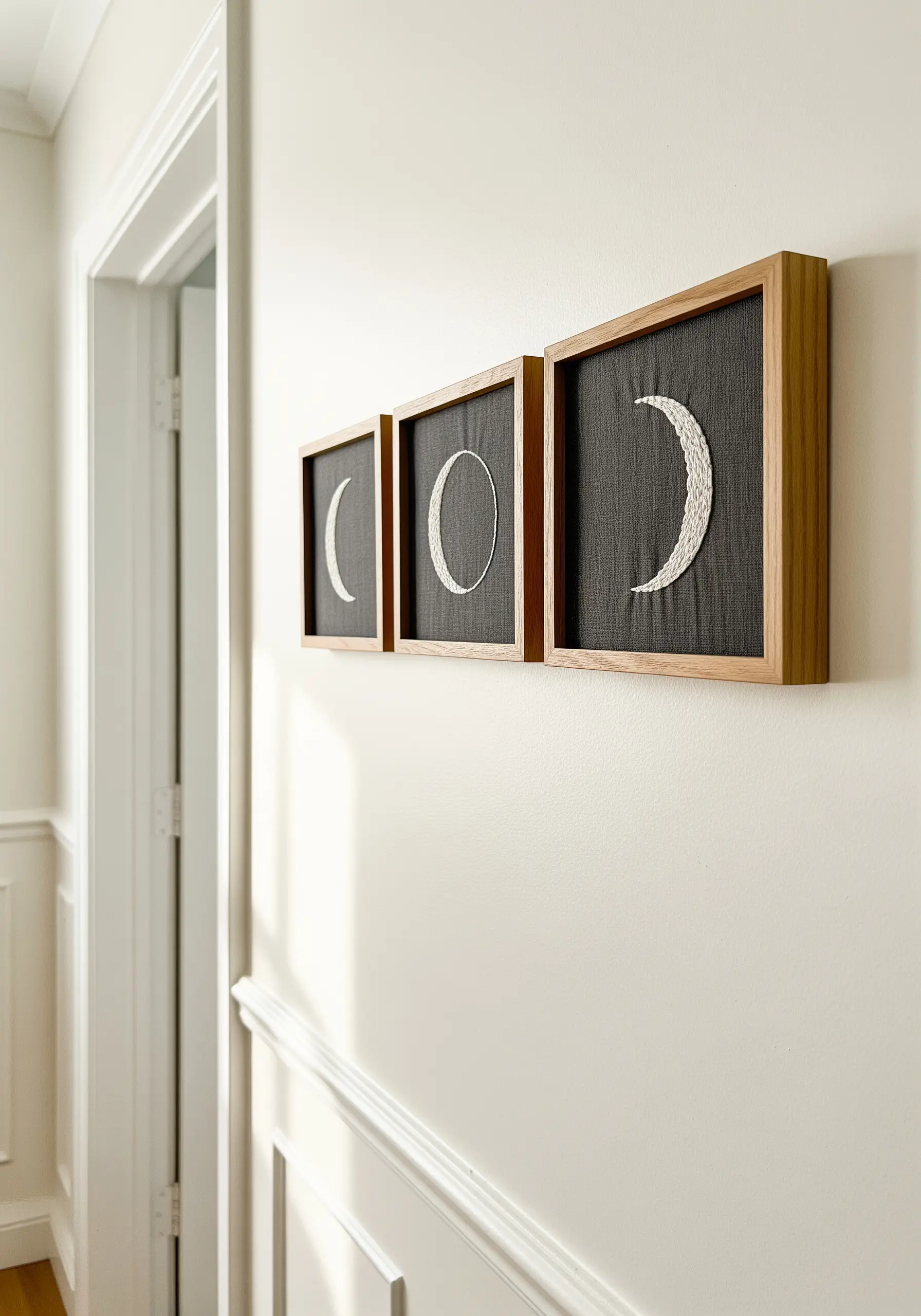 A triptych of three framed embroideries showing the phases of the moon.