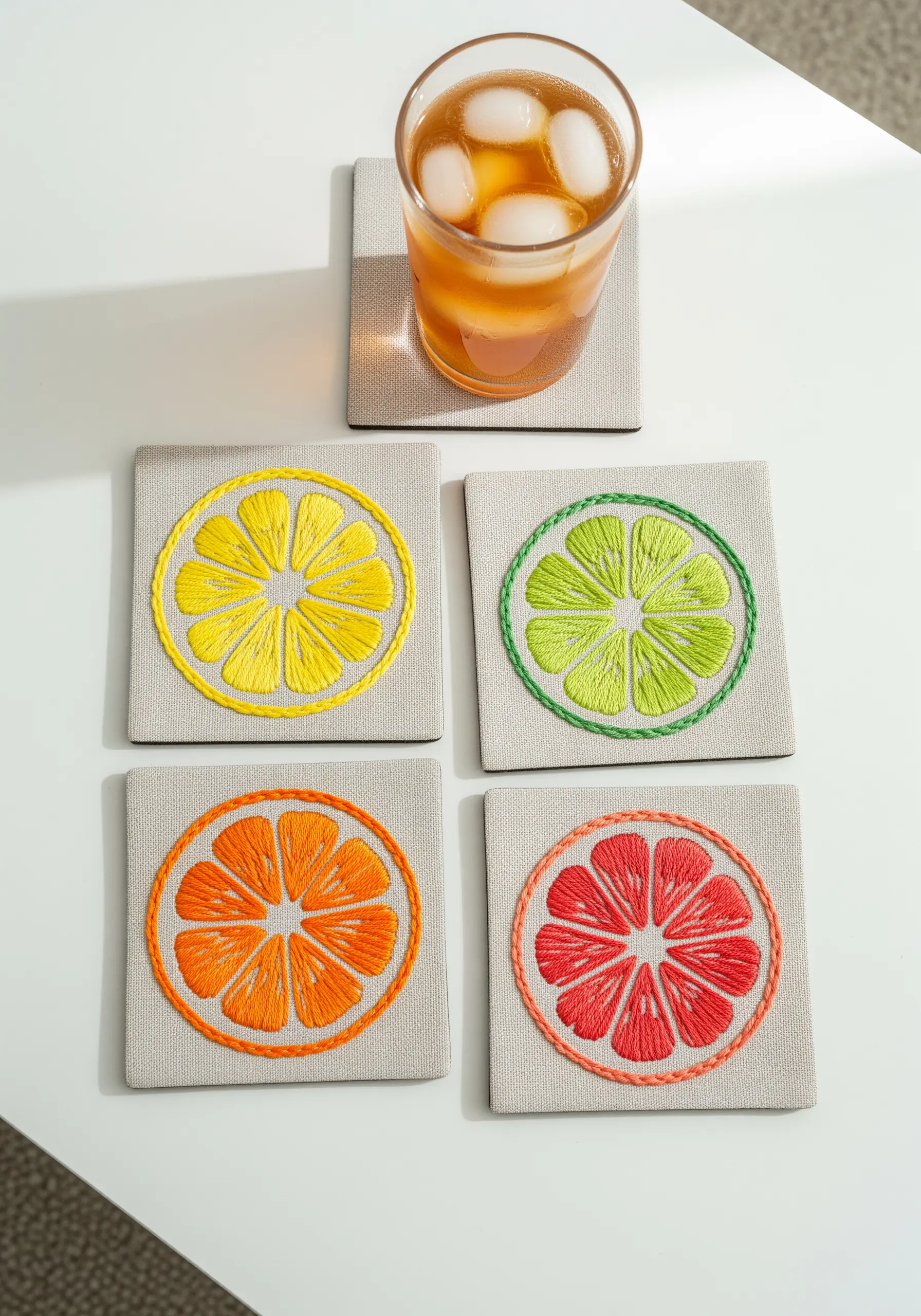 Four embroidered coasters designed as colorful slices of lemon, lime, orange, and grapefruit.