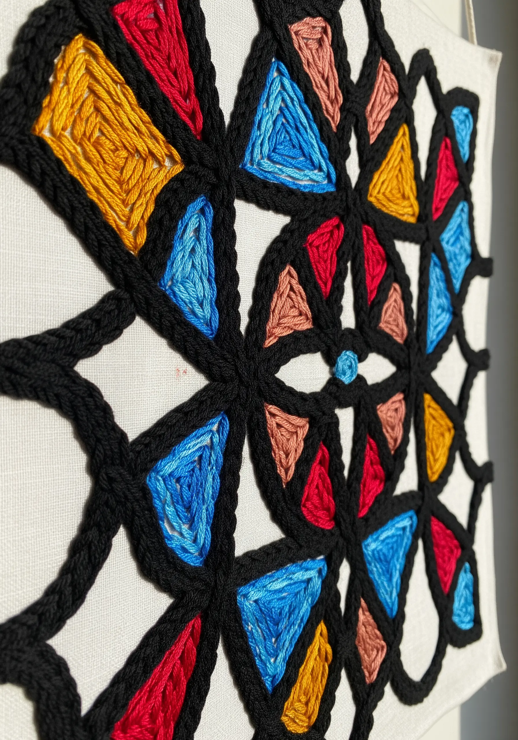 Close-up of a geometric embroidery with thick black outlines and vibrant color fills.