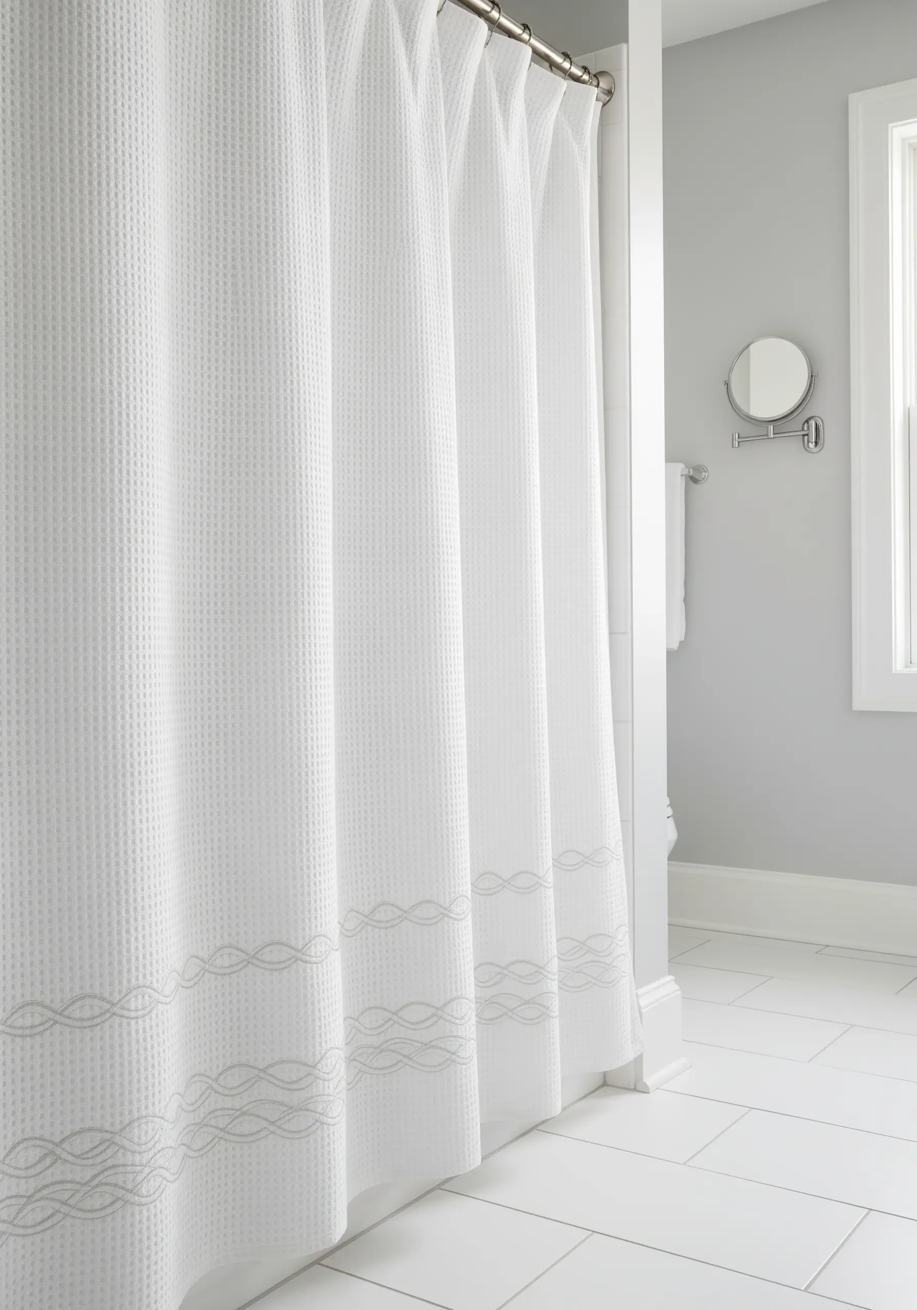 A simple, tonal wave pattern embroidered along the bottom of a white shower curtain.