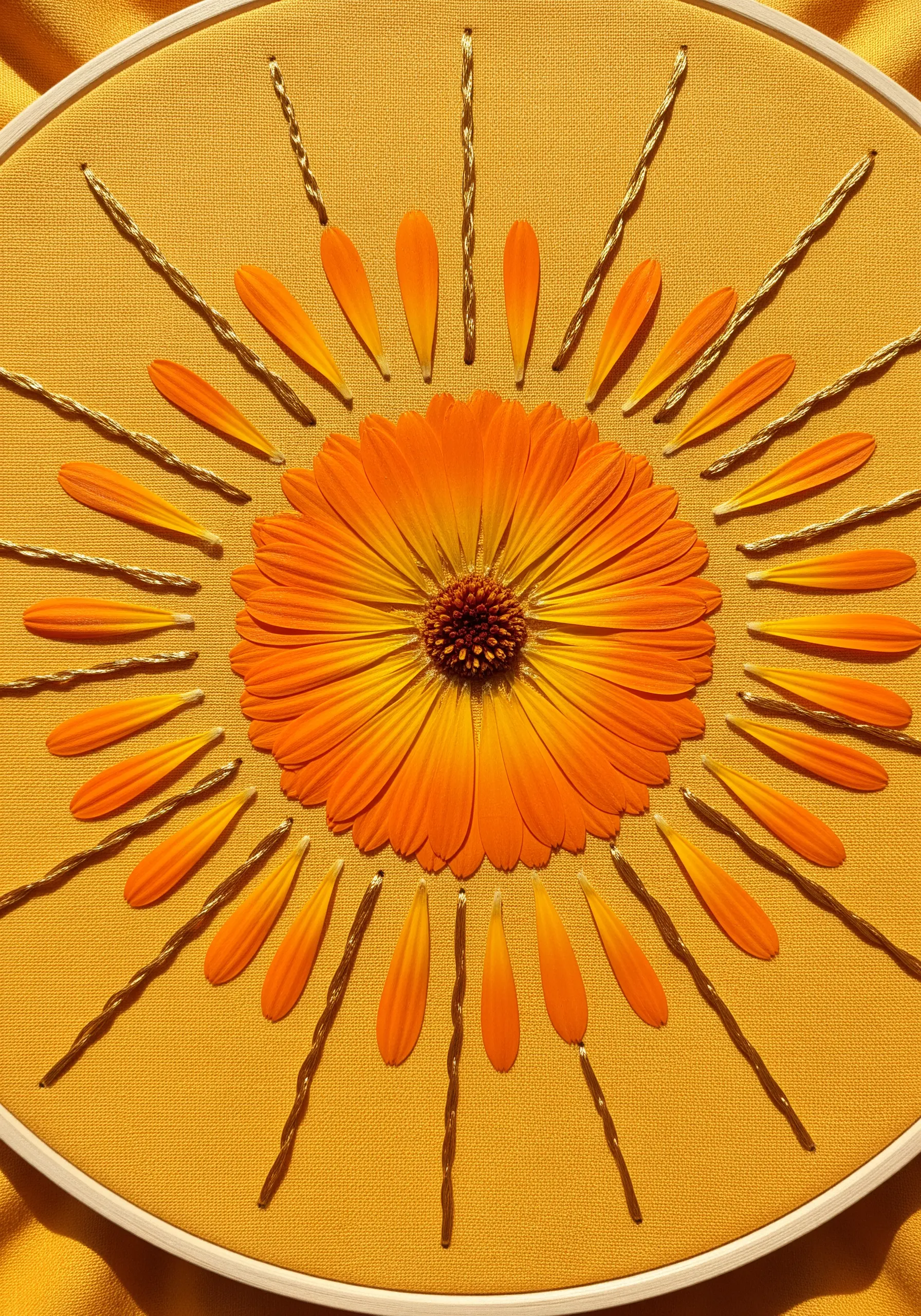 A sunburst design using a pressed calendula flower, petals, and gold thread.