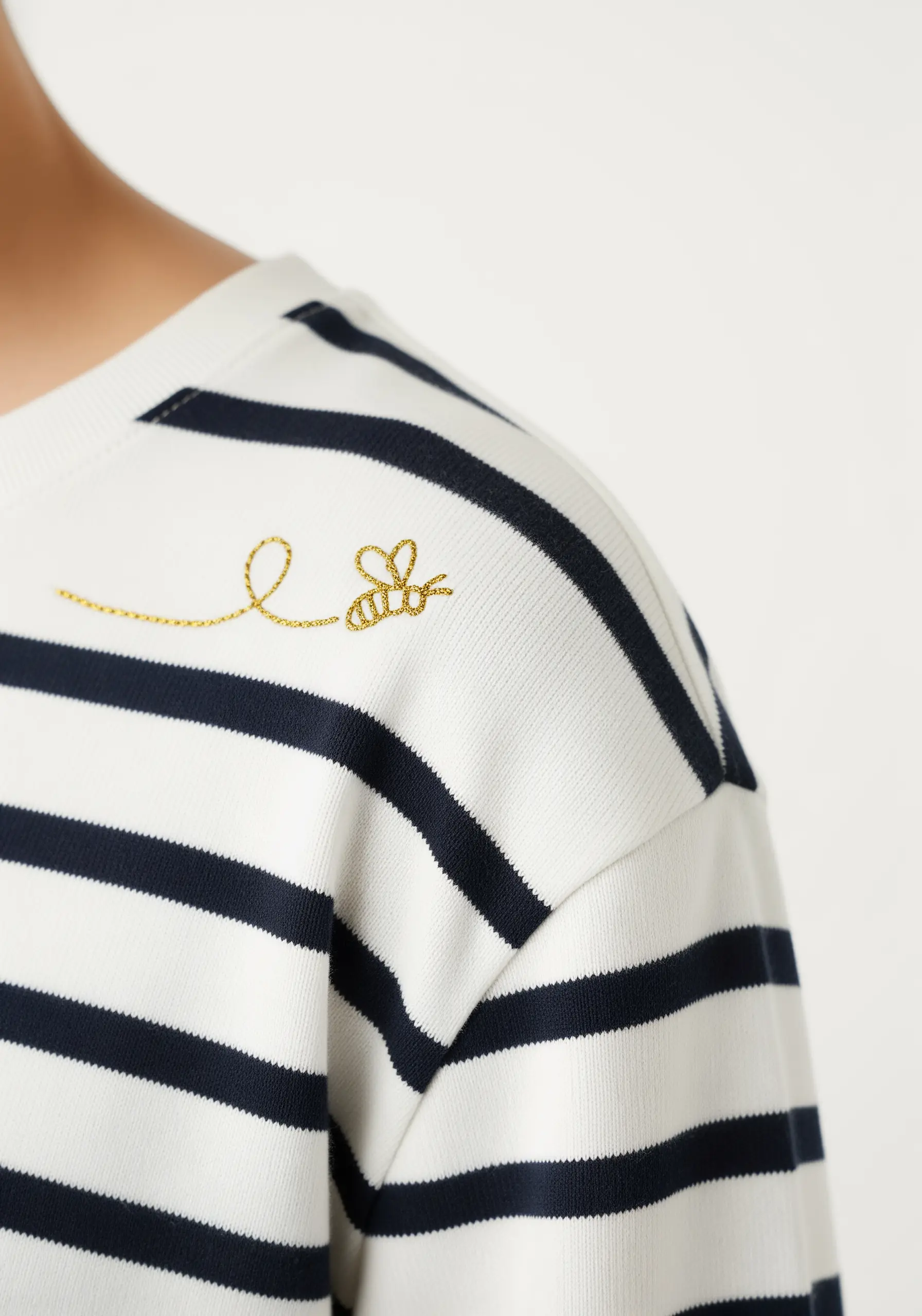 A tiny bee with a shimmering gold flight path embroidered on a striped sweater.