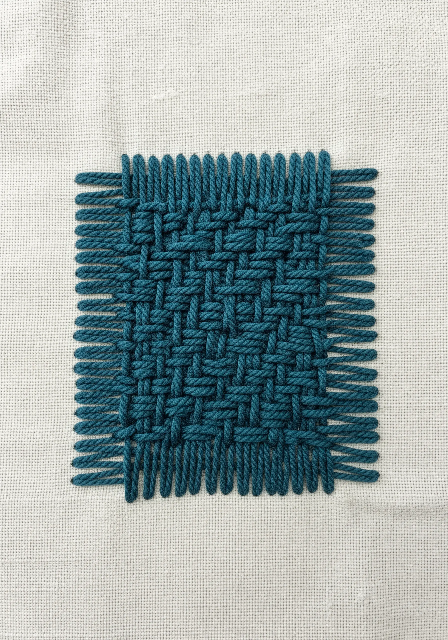 A square patch of woven teal threads on a plain off-white embroidery canvas.