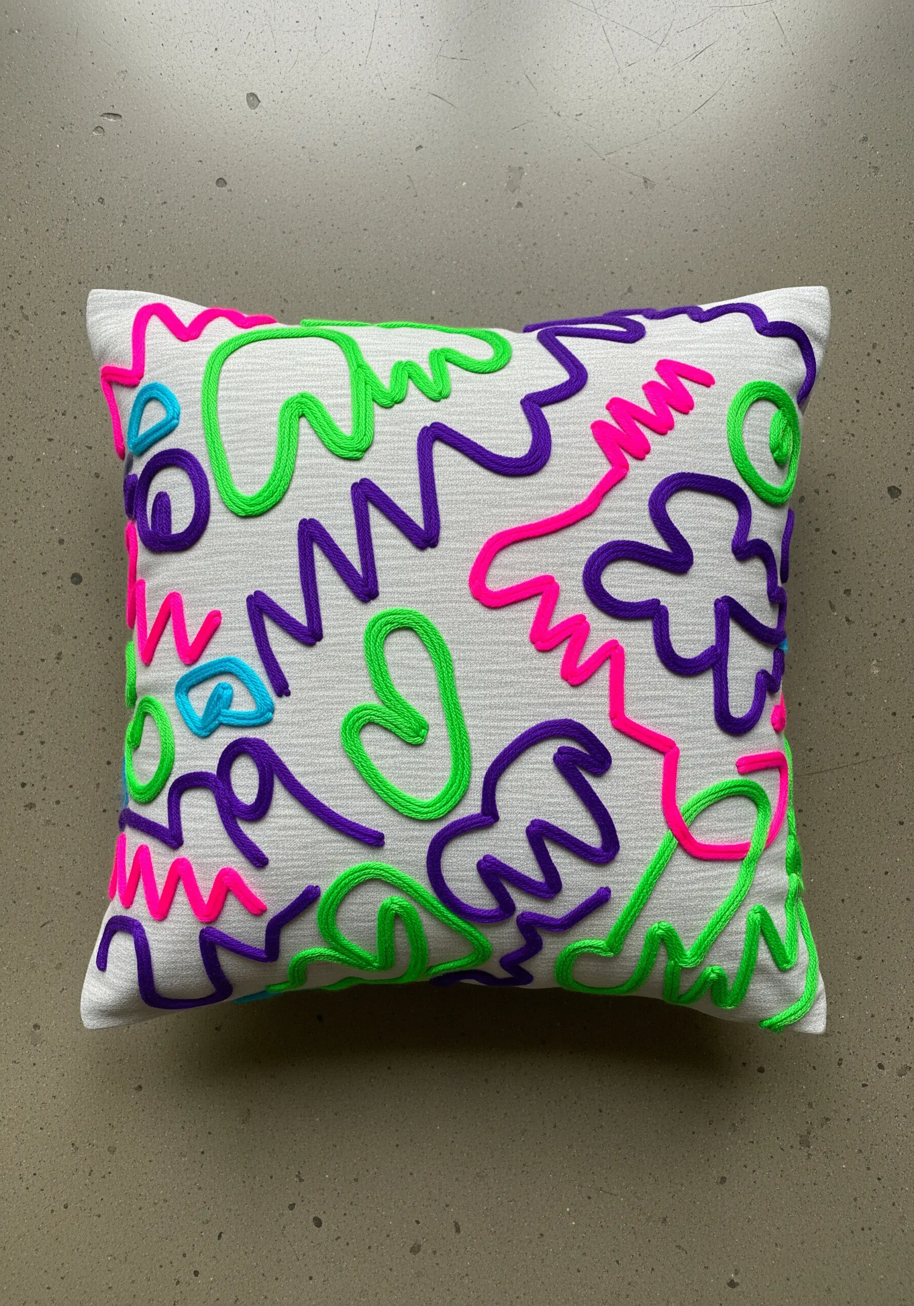 Abstract neon doodles in raised stem stitch on a white textured pillow.