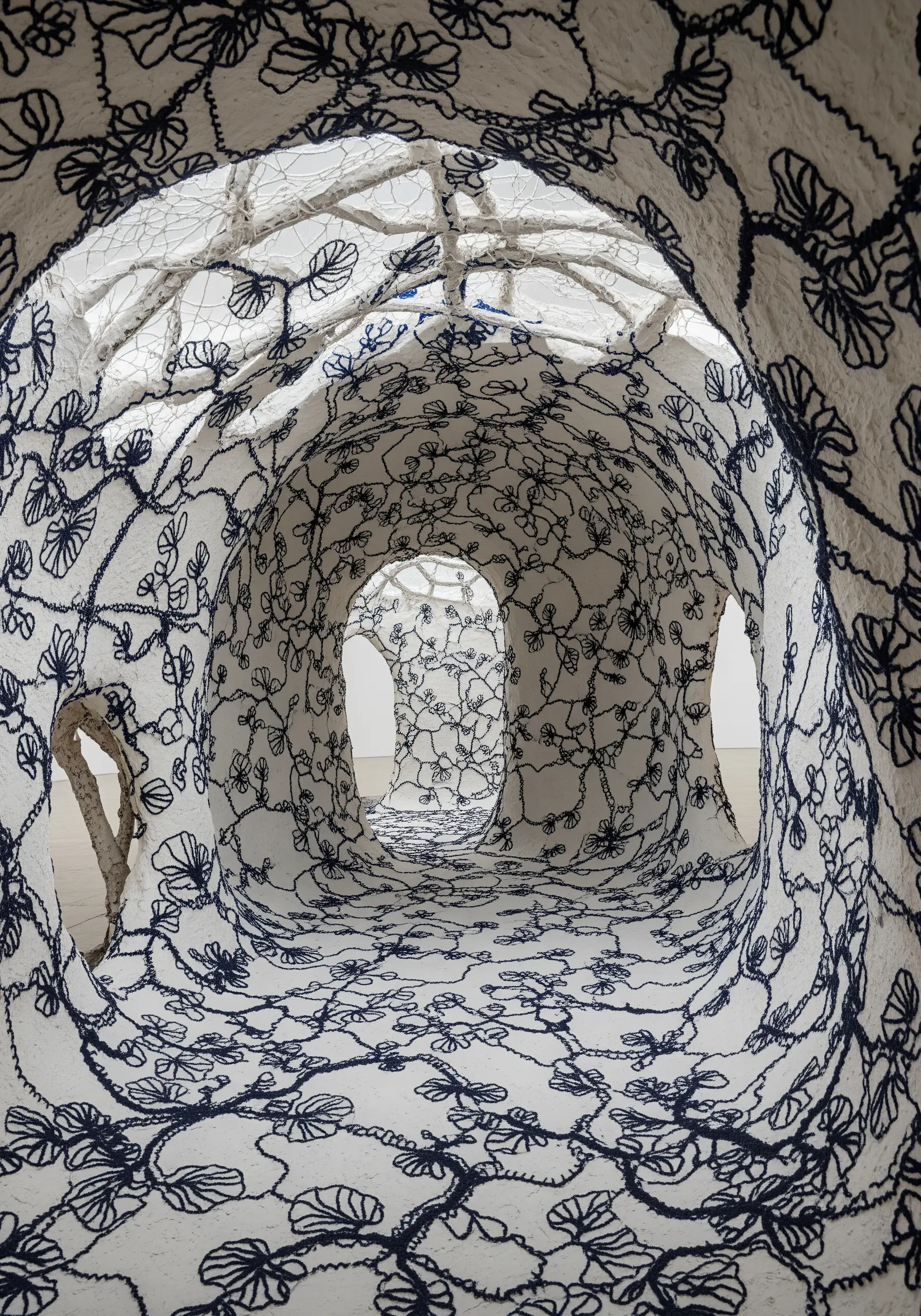 The interior of a cave-like sculpture entirely covered in white fabric with dense black embroidery.