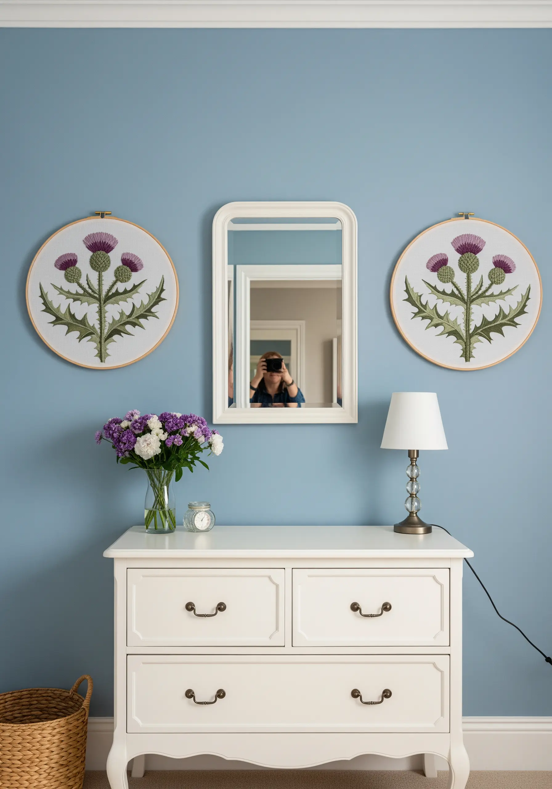 Two identical embroidery hoops of Scottish thistles flanking a white mirror over a dresser