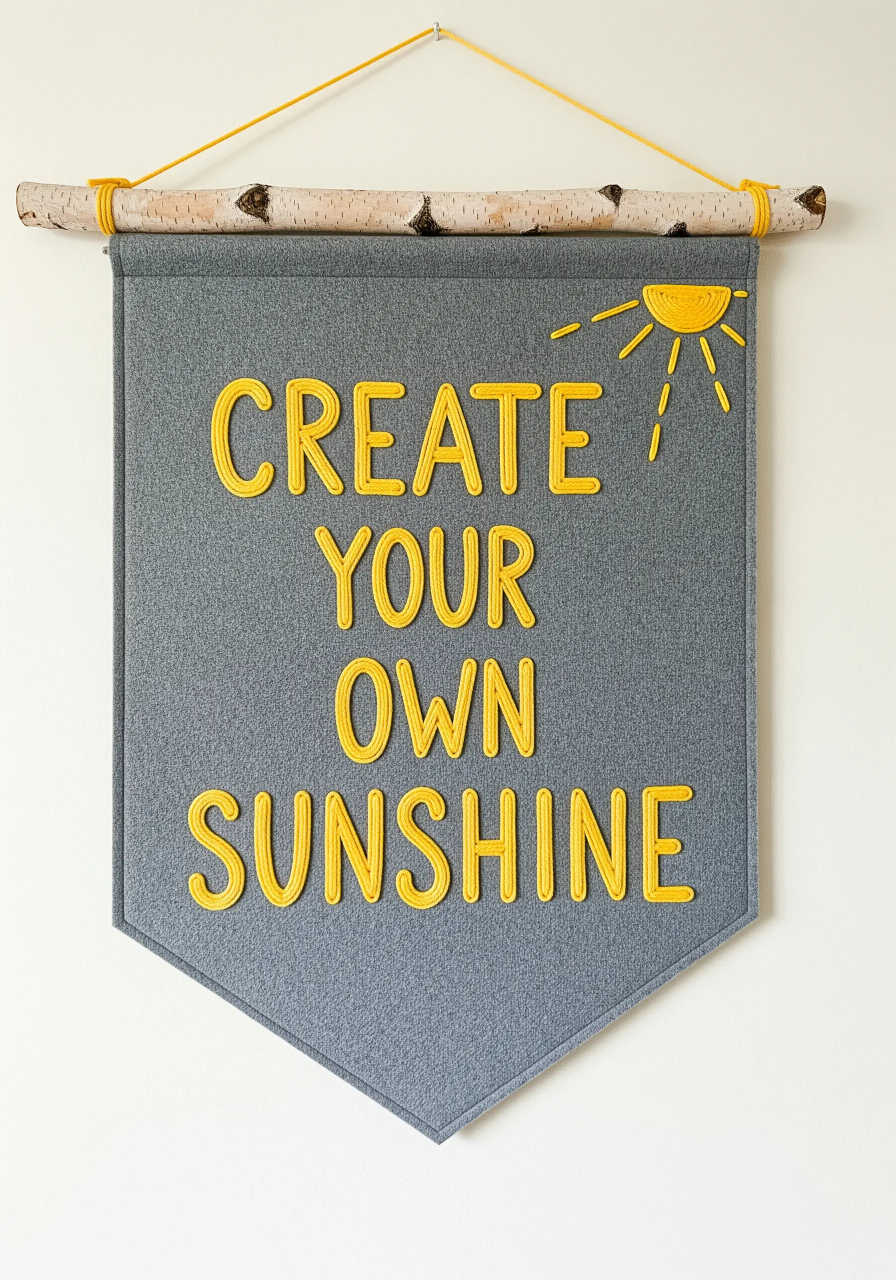 A grey felt banner with the quote 'CREATE YOUR OWN SUNSHINE' stitched in yellow yarn.