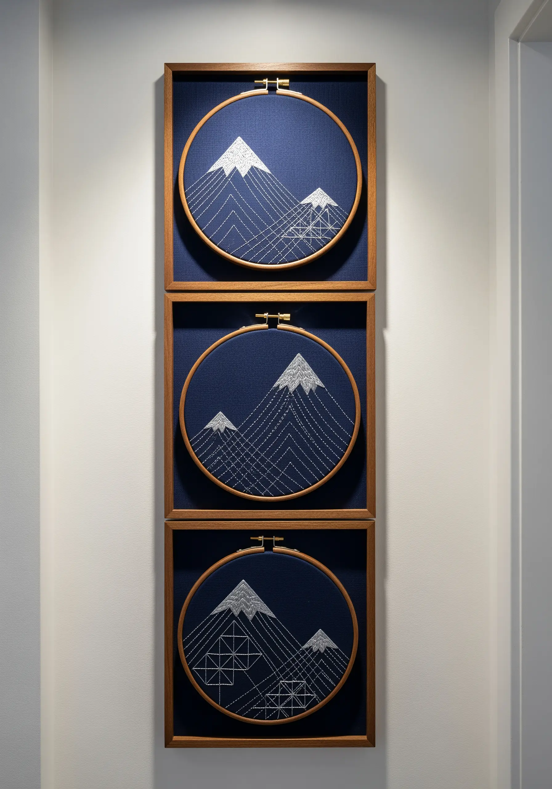 Triptych of geometric mountain embroidery in minimalist gallery frames.