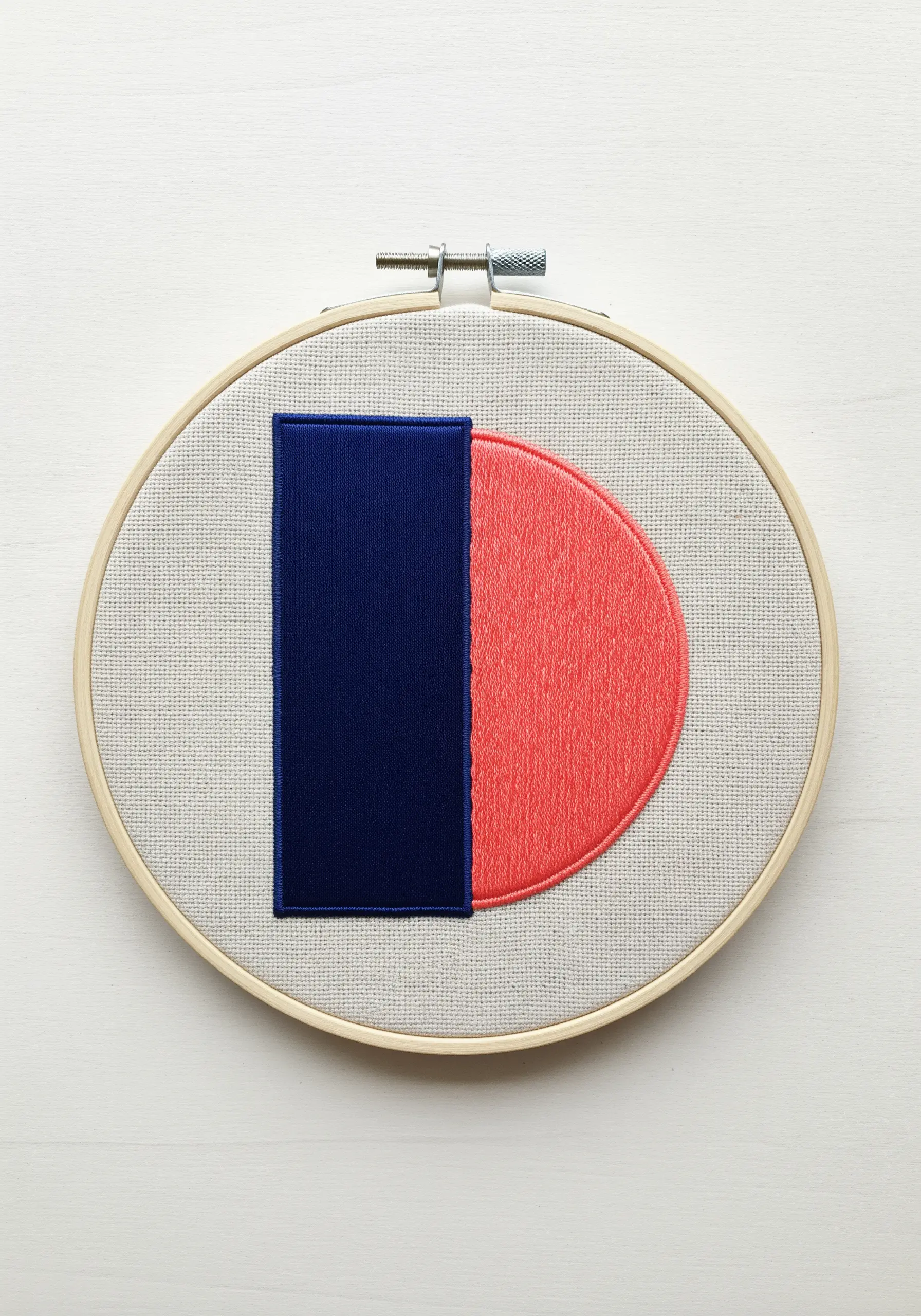An abstract geometric shape in an embroidery hoop with a crisp edge between navy and coral satin stitch.