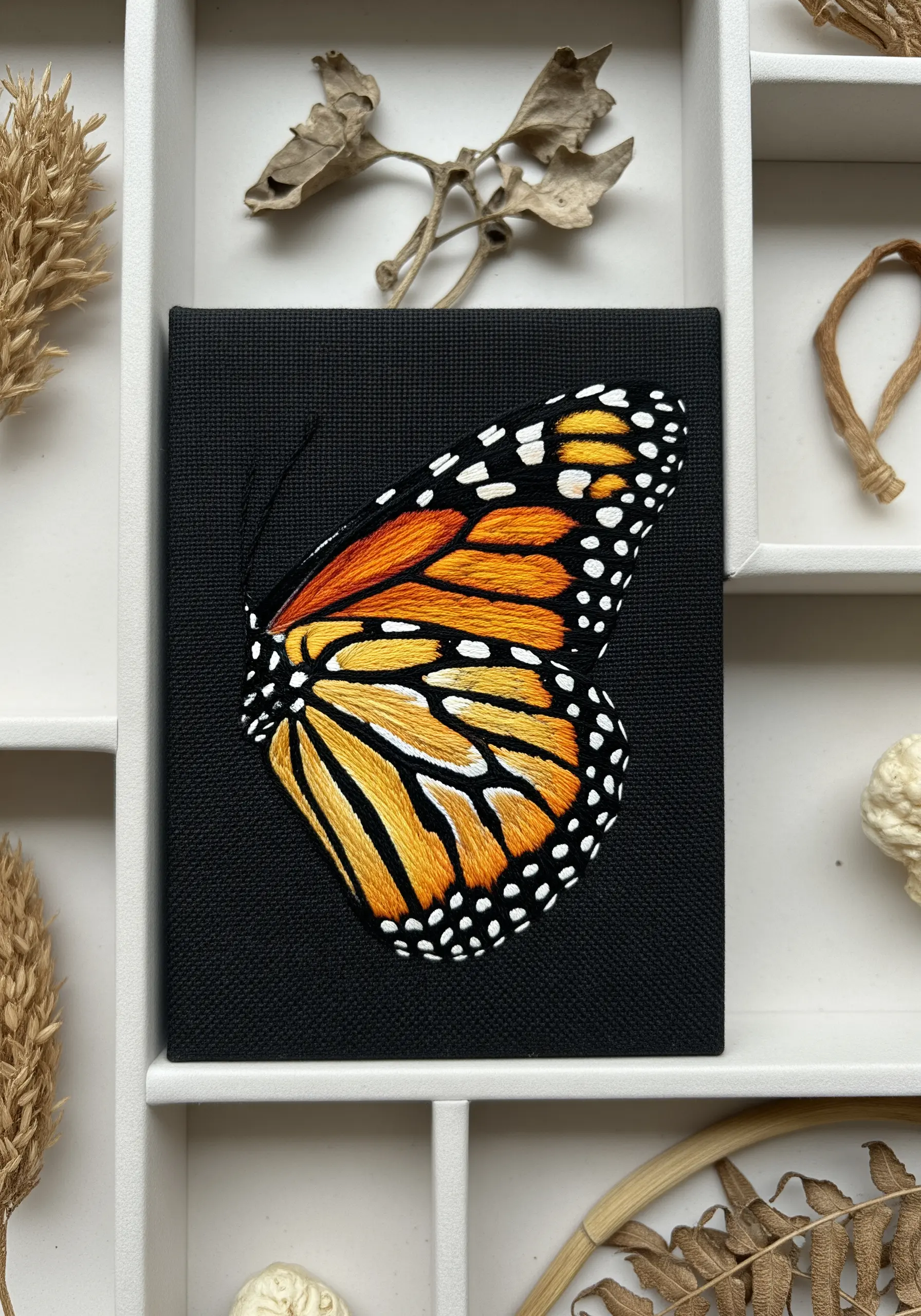 A vibrant monarch butterfly wing embroidered with clean satin stitch on black canvas.