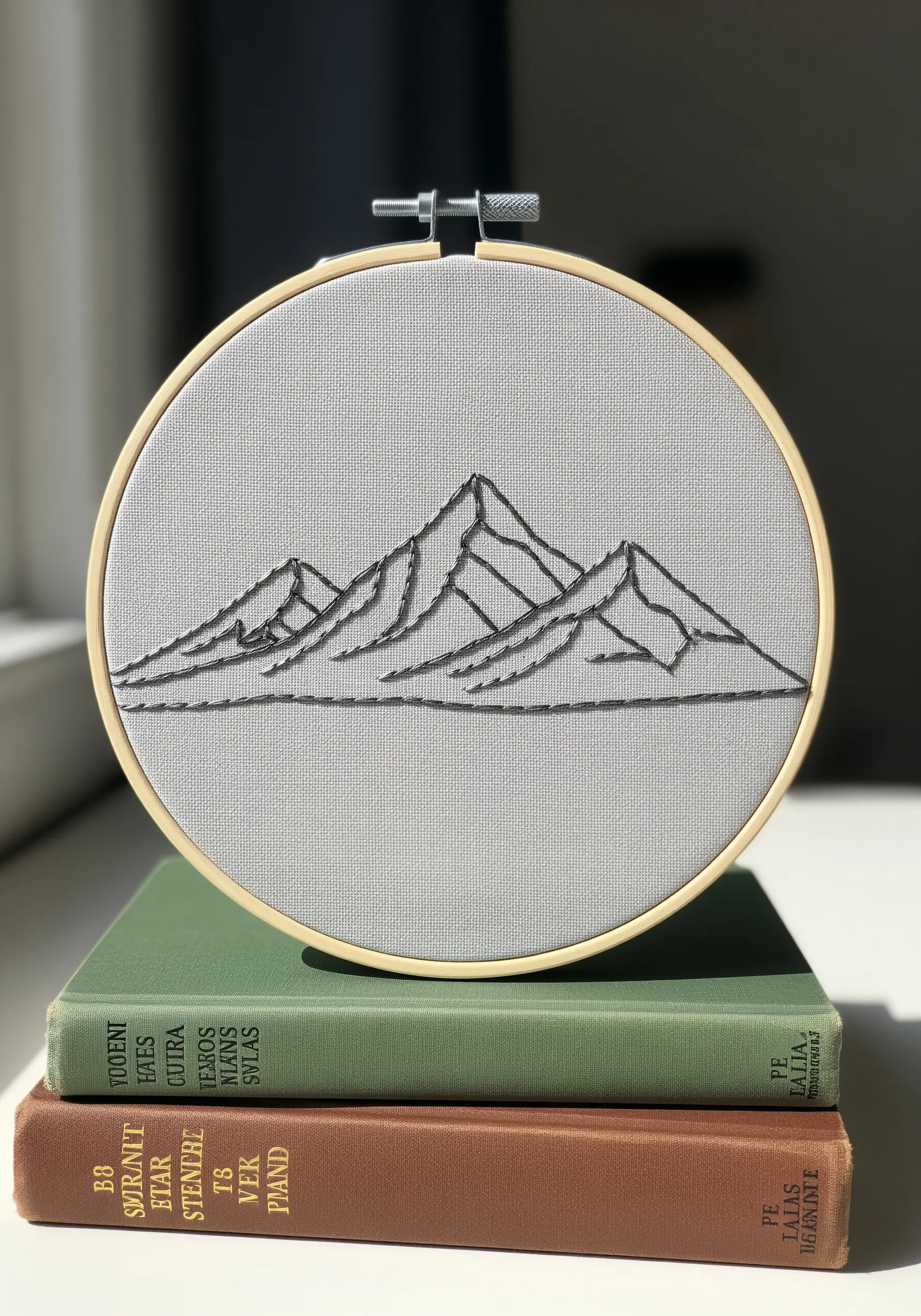 A minimalist mountain range embroidered in dark gray thread on light gray fabric.