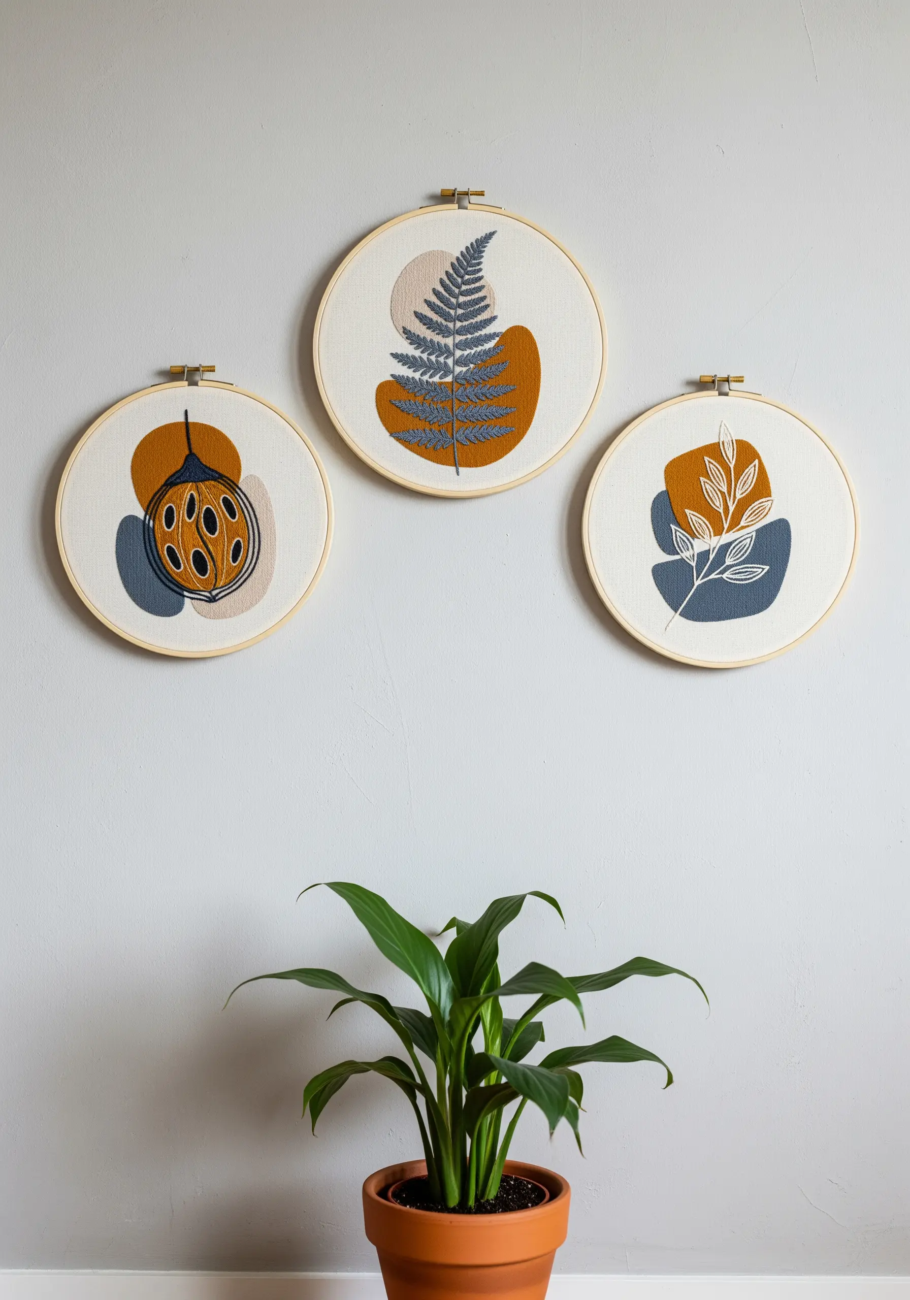 A trio of embroidery hoops with botanical motifs over abstract fabric appliqué shapes.