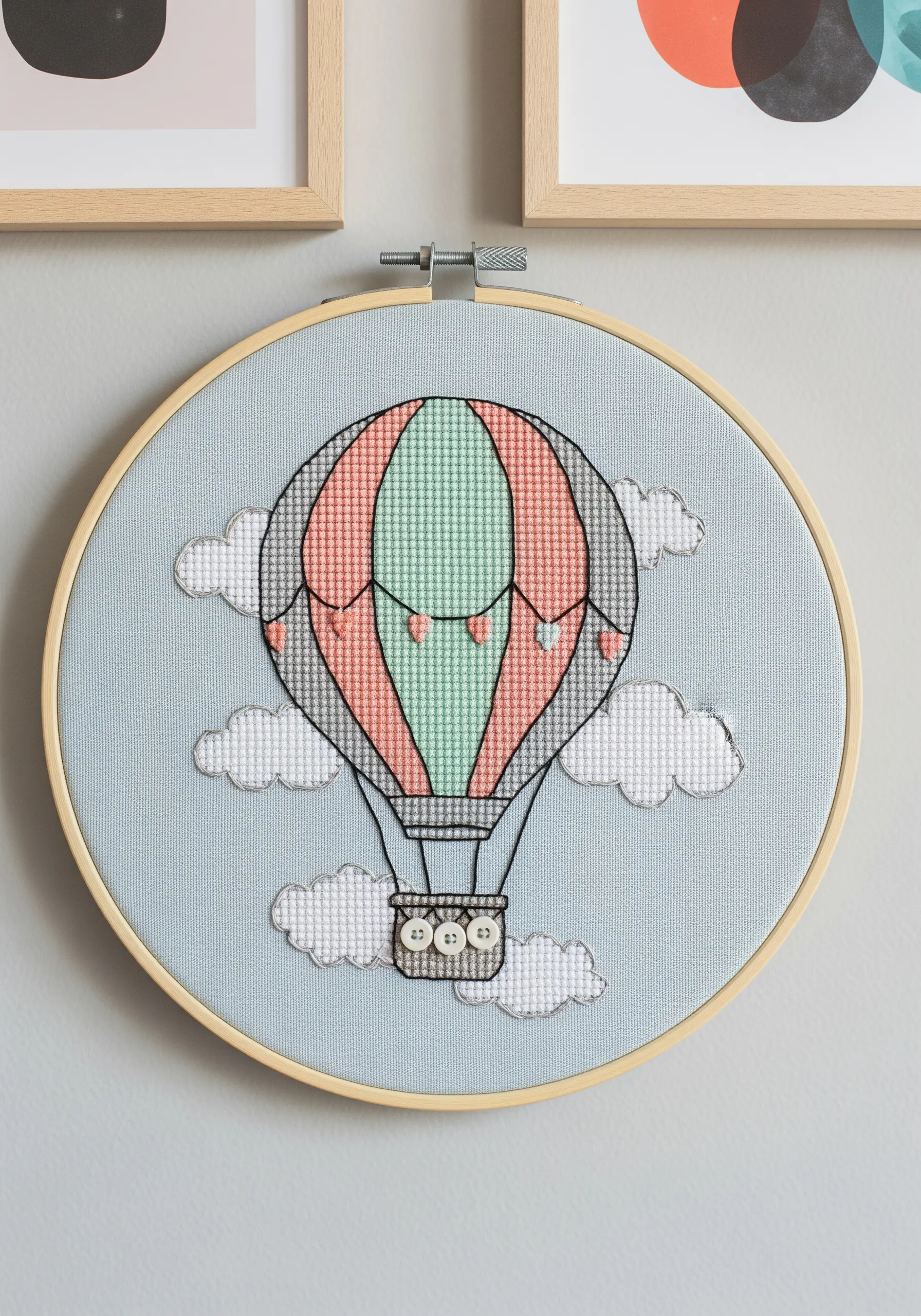 A cross-stitched hot air balloon appliquéd onto a light blue background with fluffy clouds.