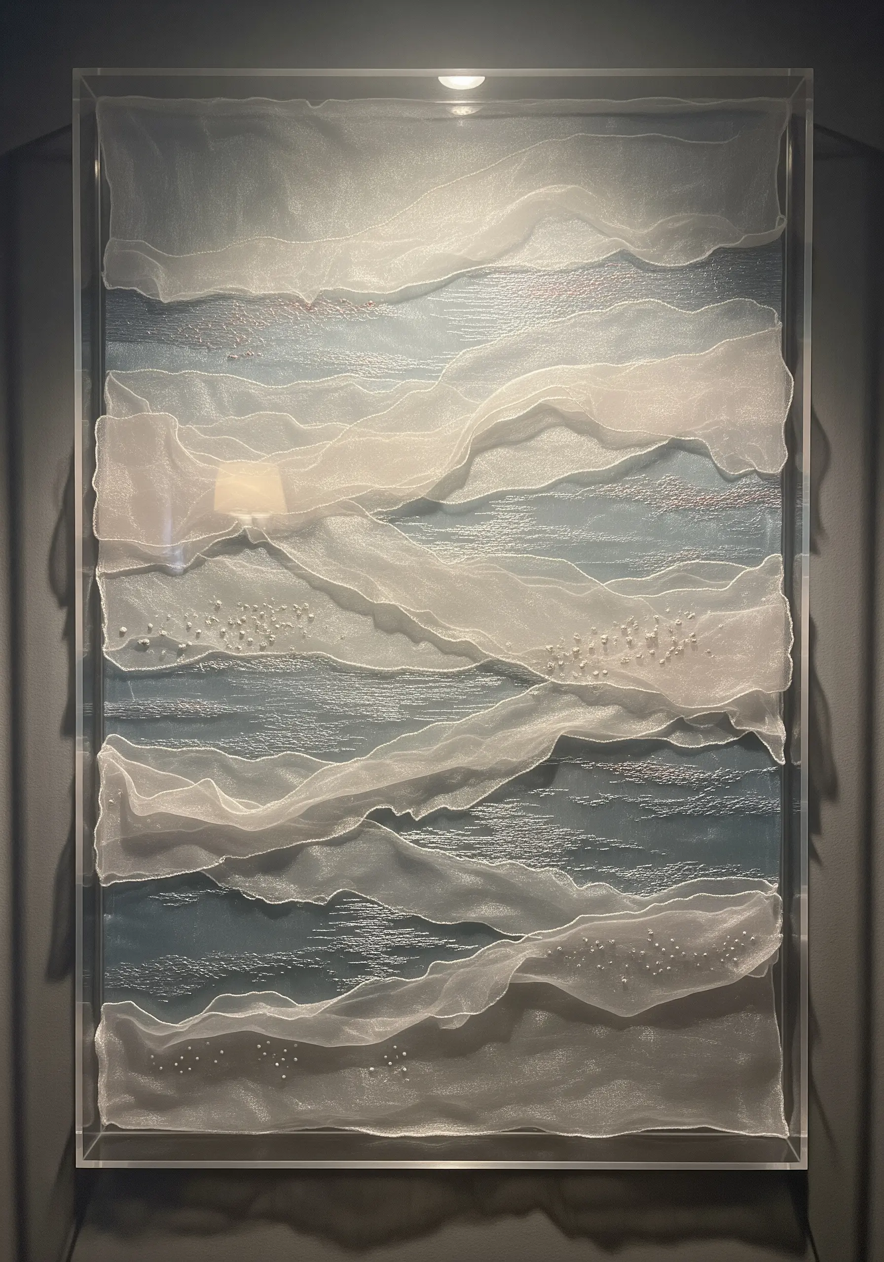 Abstract textile art in a clear box frame with layers of sheer white fabric over a blue base.