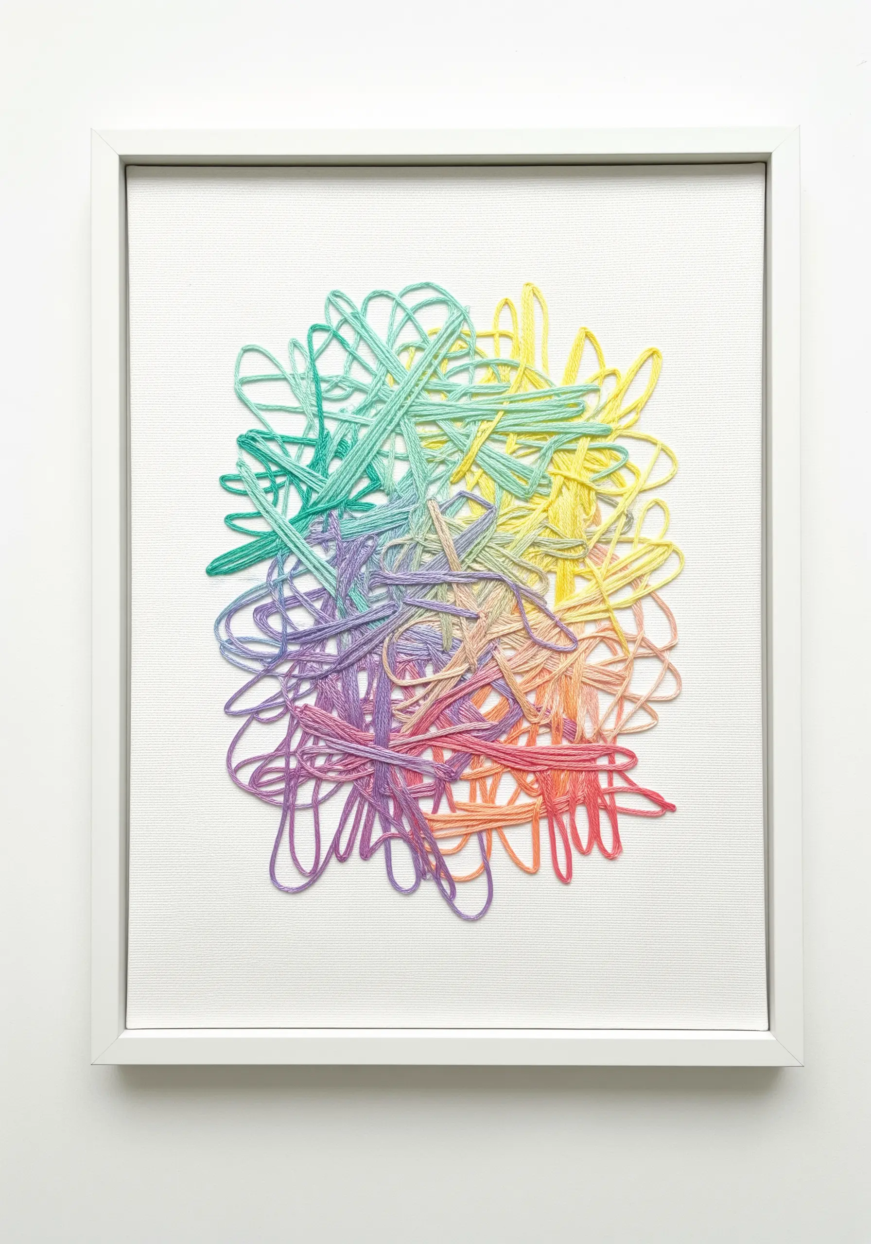 A framed abstract piece made of tangled, multicolored yarn couched onto a white canvas.
