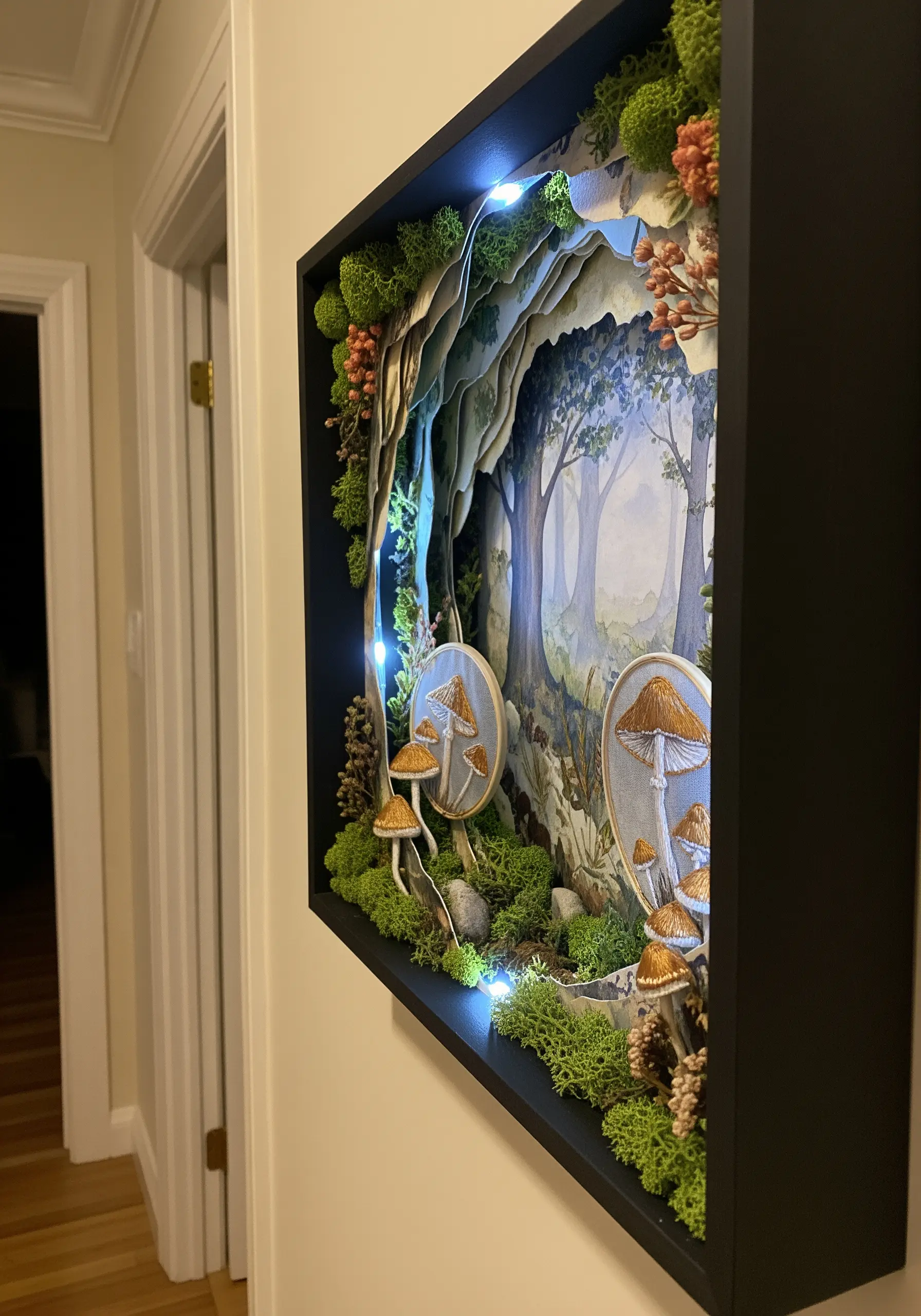 A 3D shadow box art piece with embroidered mushrooms, layered paper, and soft LED lights.