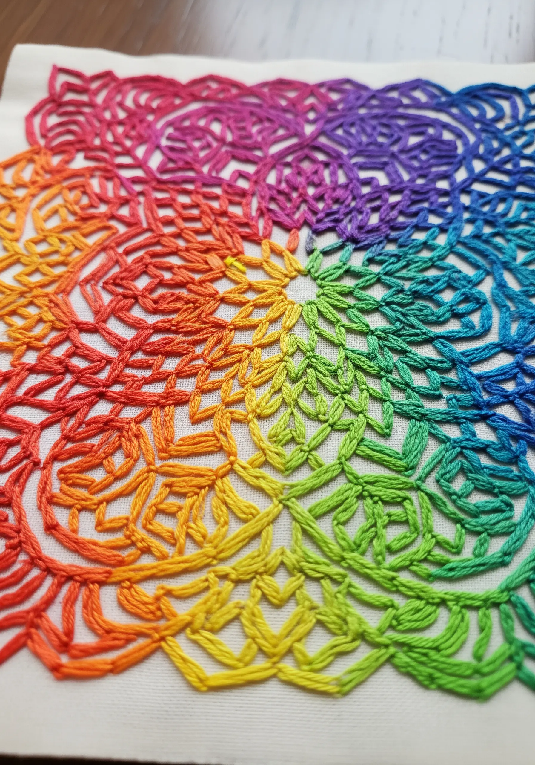 A close-up of a complex geometric pattern filled with a rainbow gradient of chain stitches.