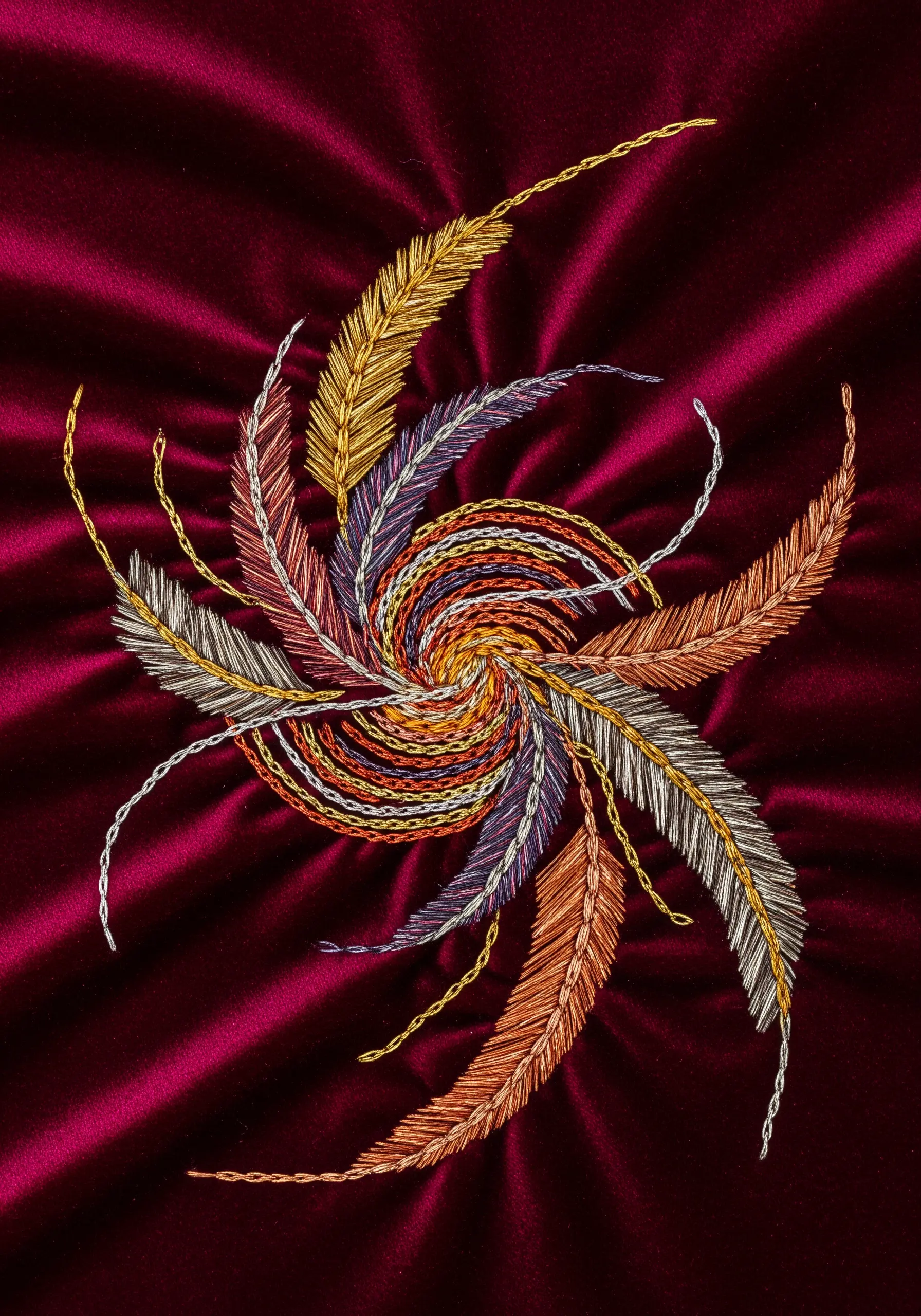 Swirling, feather-like shapes embroidered in metallic threads on a rich, dark red velvet fabric.