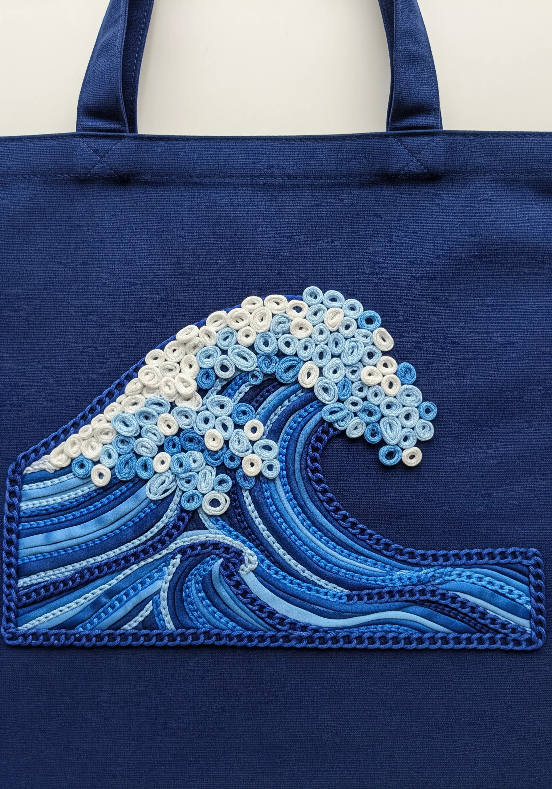 An embroidered wave made with rolled fabric coils, chain stitches, and satin stitches.