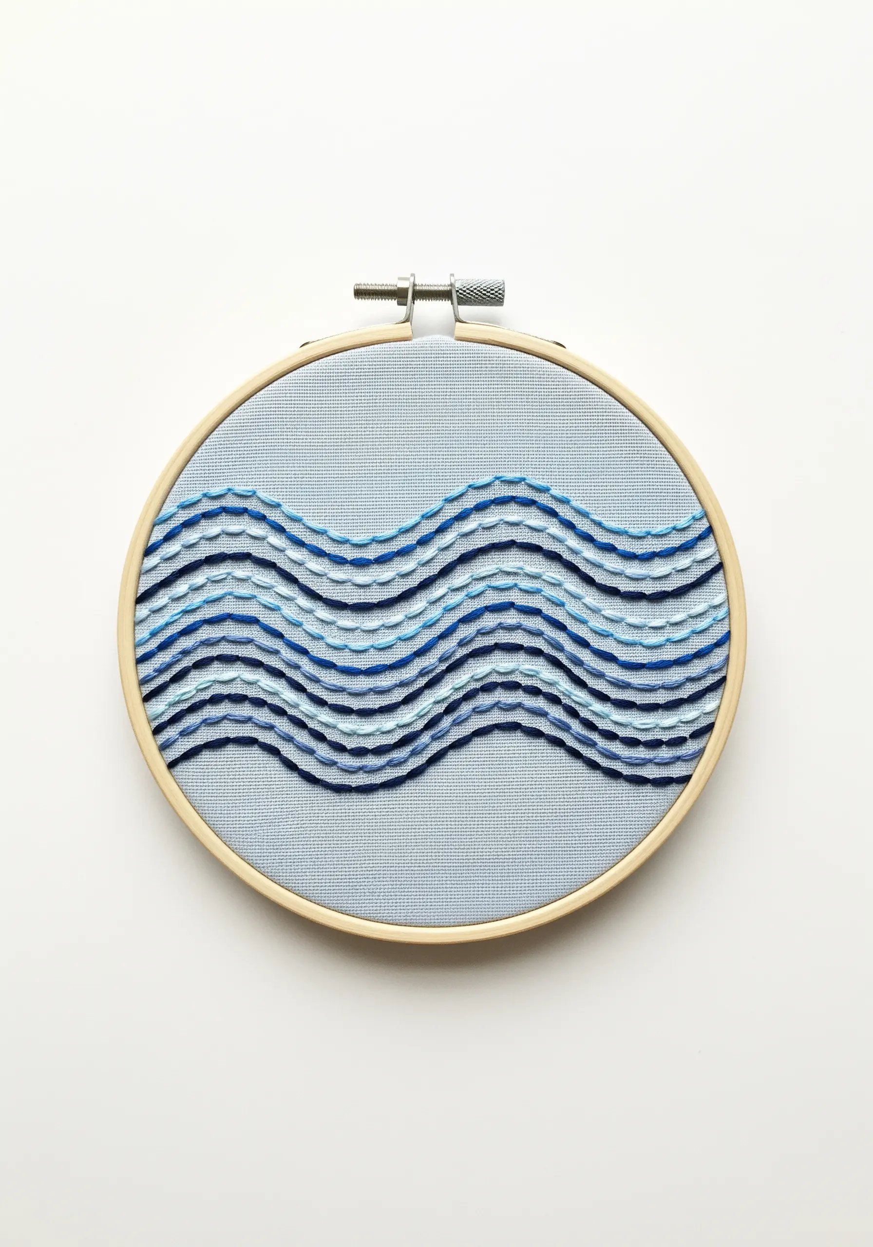 Abstract ocean waves embroidered with layered stitches in shades of blue.