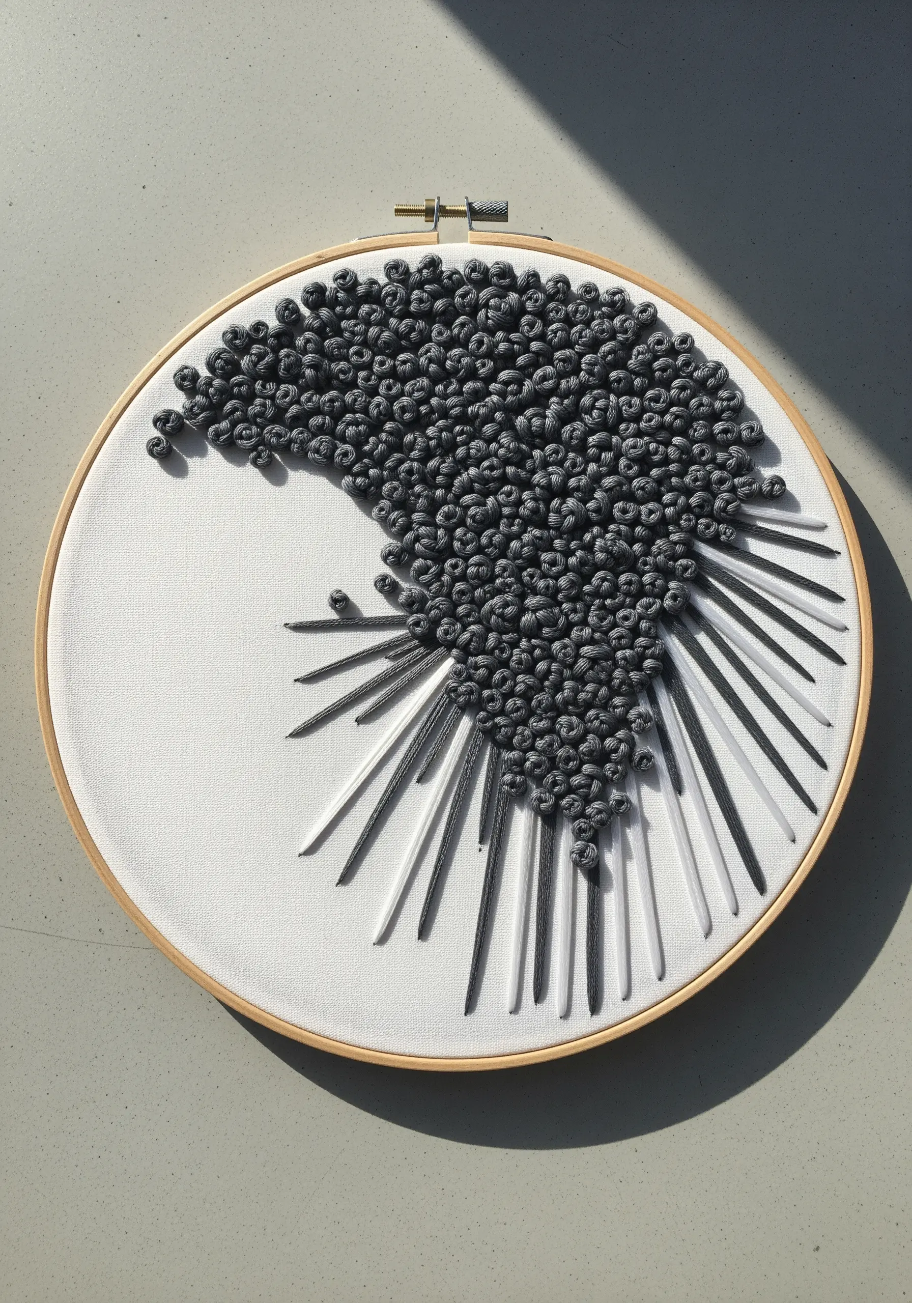 Abstract hoop art with dense grey French knots and radiating straight stitches.