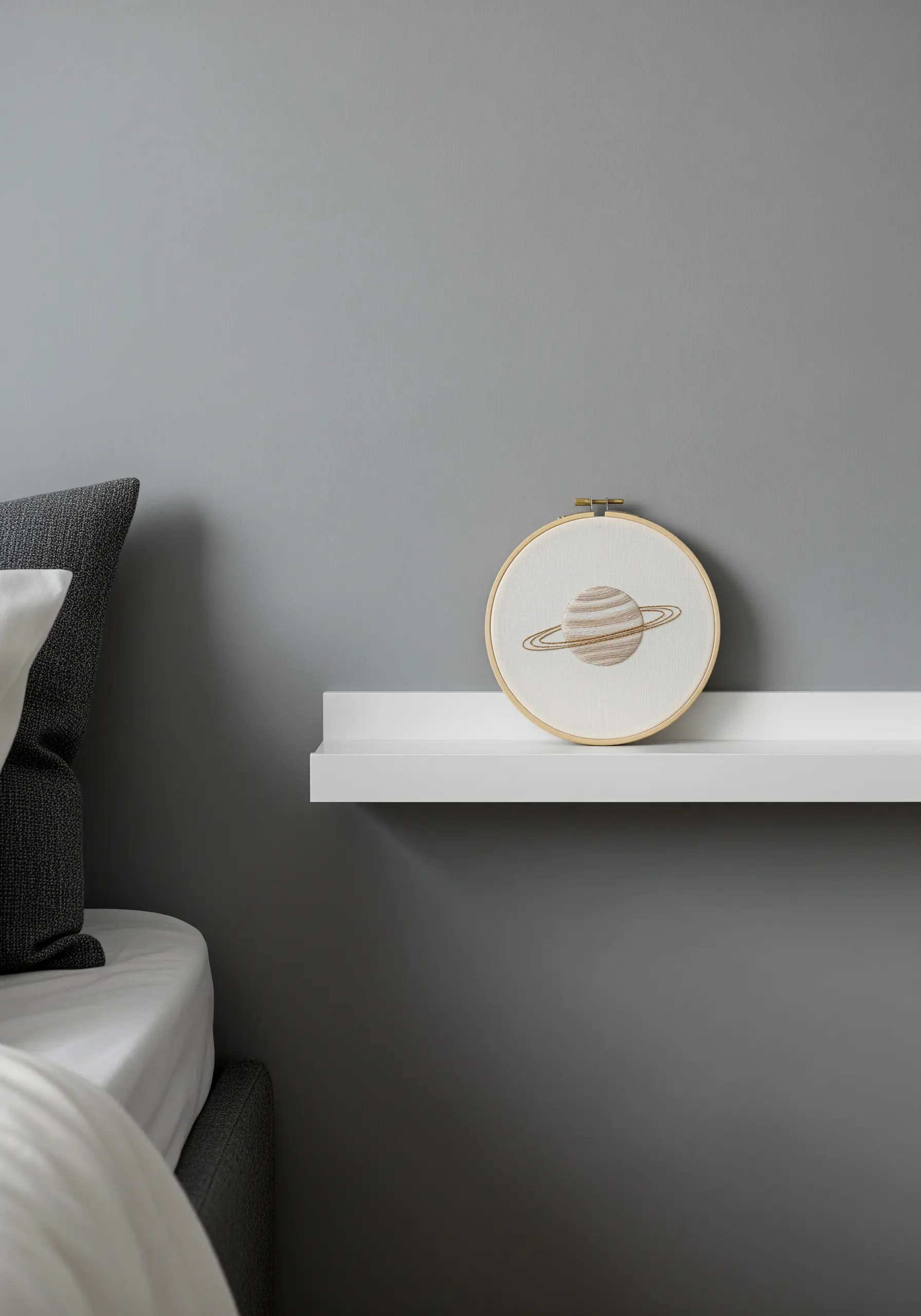 A small embroidery of the planet Saturn displayed on a floating white shelf.