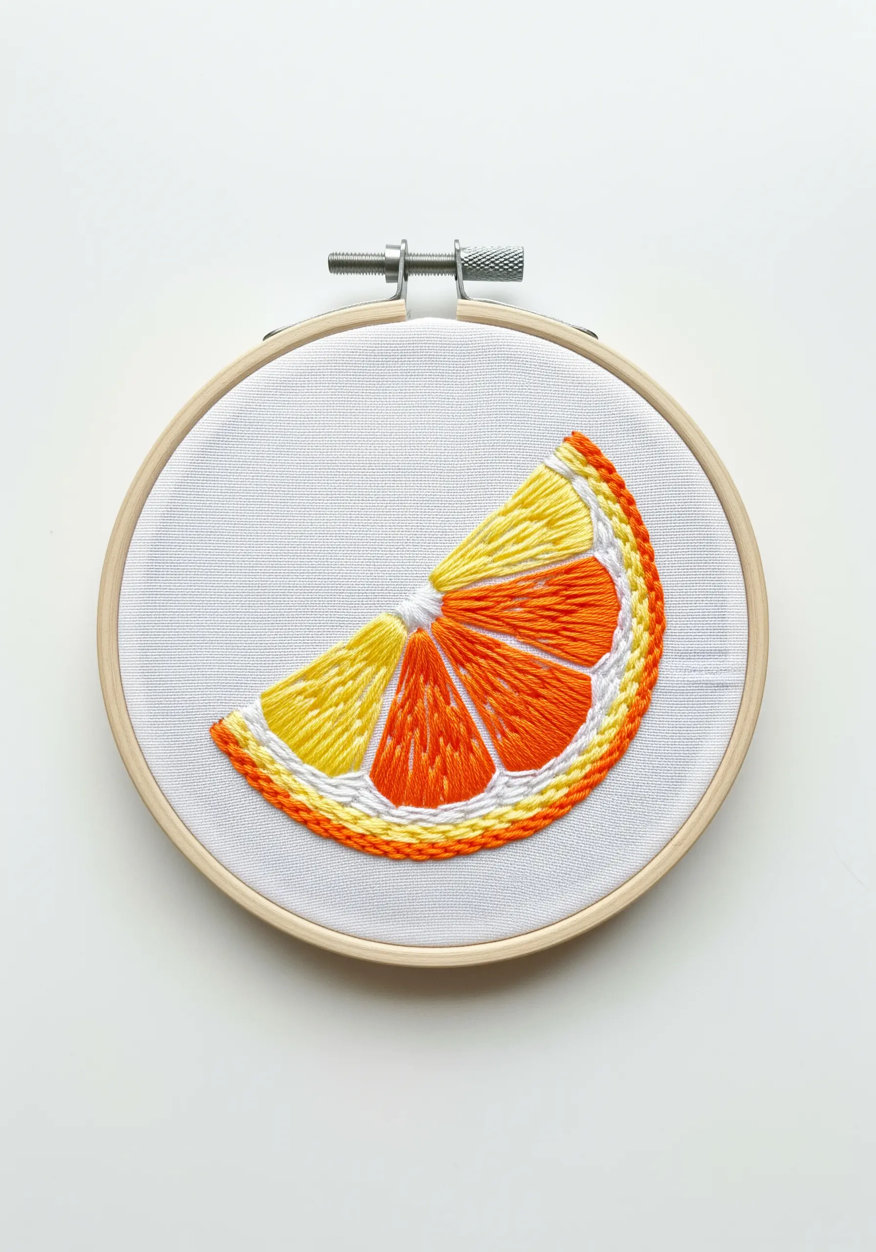An embroidered citrus slice with directional satin stitch and a textured rind.