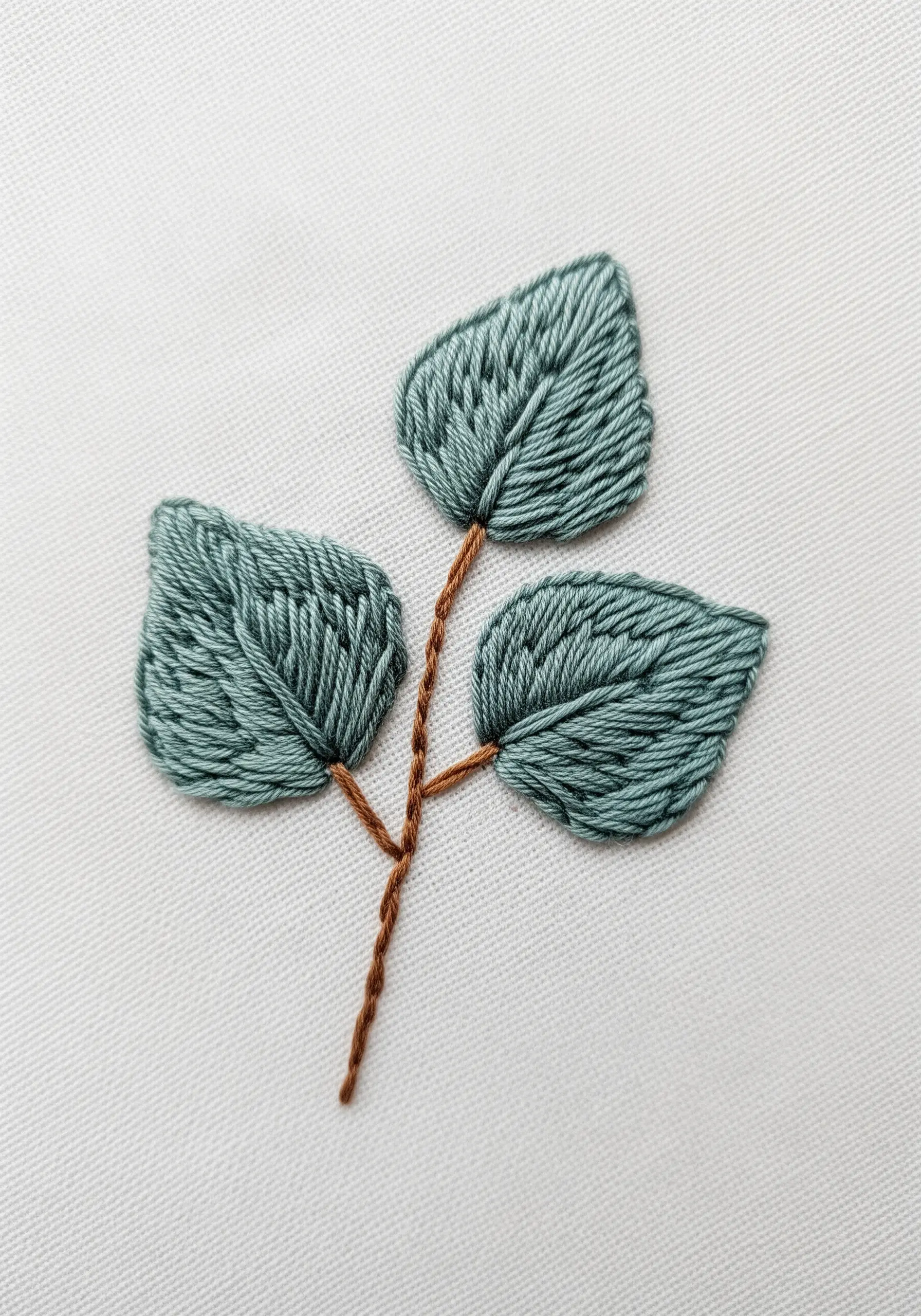 A close-up of three embroidered leaves in dusty green, showcasing the fishbone stitch technique.